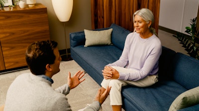 Male receptionist greeting a female patient in a healthcare waiting area.