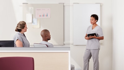 Three nurses having a meeting within a prefab light ash, woodgrain laminate Commend Nurses Station