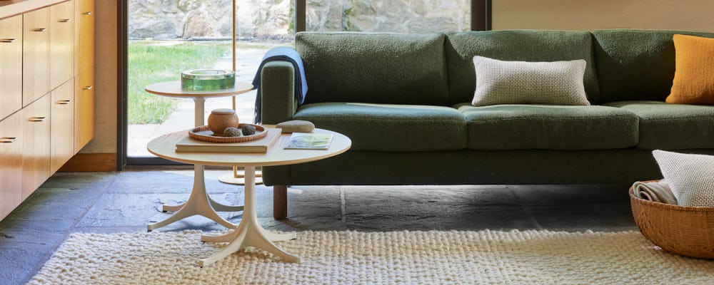Environment of three seater Lispenard Sofa in dark green fabric and 6" walnut legs with and Nelson Tables.