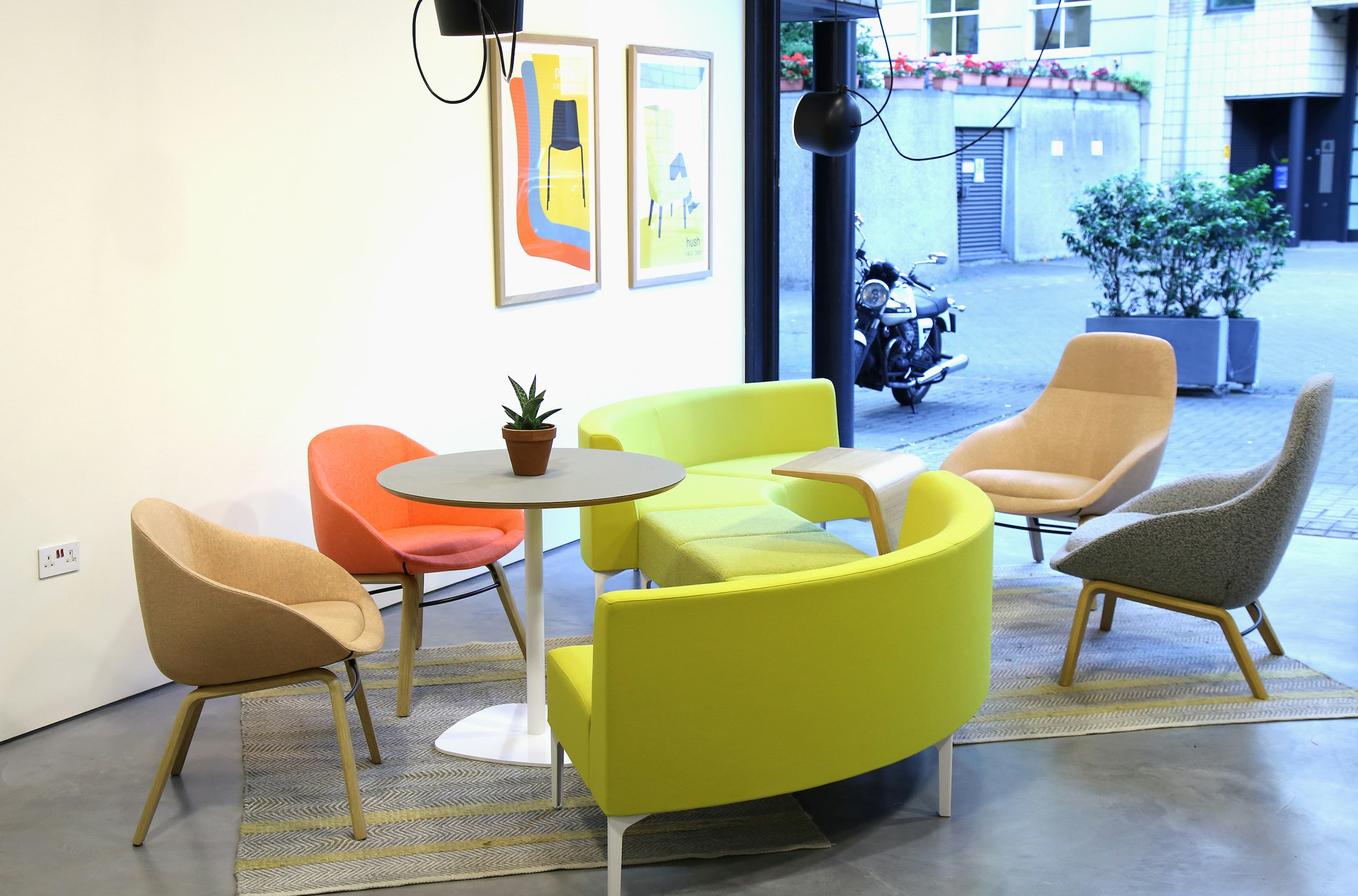 A Ped Café Table with a gray top and white base uniting two Always Lounge Chairs and a lime green Symbol Modular Seating unit.