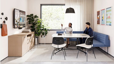 A group setting featuring two people sitting on a blue corner bench while participating in a virtual meeting in a conference room furnished with Geiger Tuxedo Component Lounge seating, a Knoll Grasshopper Table, and a Knoll Florence Knoll Credenza