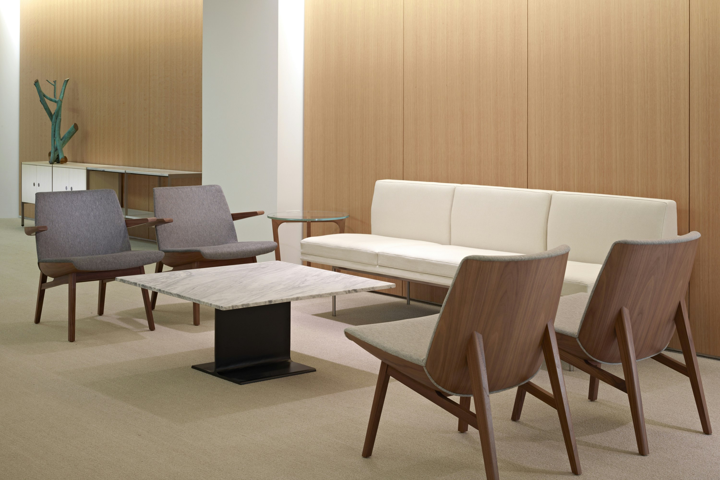 A sitting area featuring four gray Clamshell Lounge Chairs, an off-white Tuxedo Component sofa, and an I Beam occasional table.