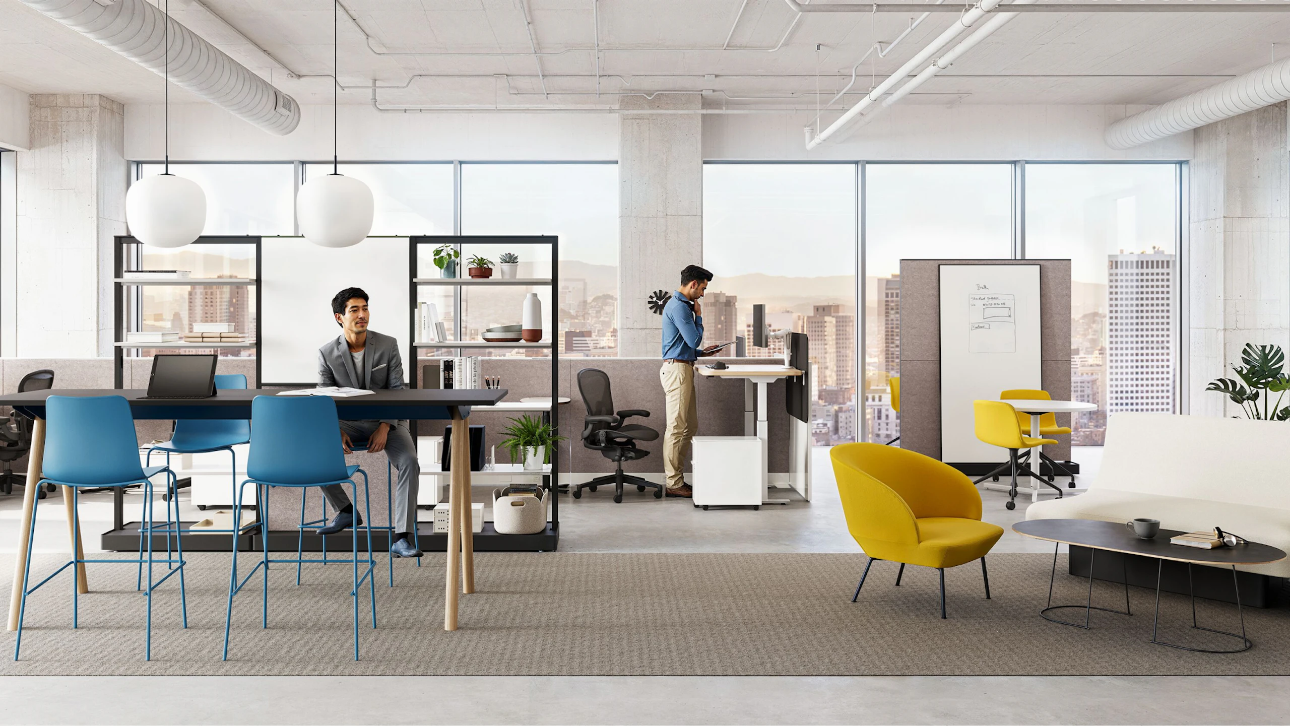 Two individuals working in a group office setting furnished with Herman Miller Passport Work Tables, NaughtOne Rhyme and Muuto Oslo Lounge boost chairs, and Herman Miller OE1 and NaughtOne Morse Bar Tables