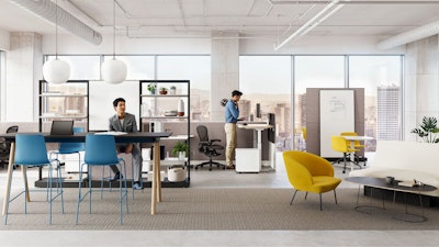 Two individuals working in a group office setting furnished with Herman Miller Passport Work Tables, NaughtOne Rhyme and Muuto Oslo Lounge boost chairs, and Herman Miller OE1 and NaughtOne Morse Bar Tables