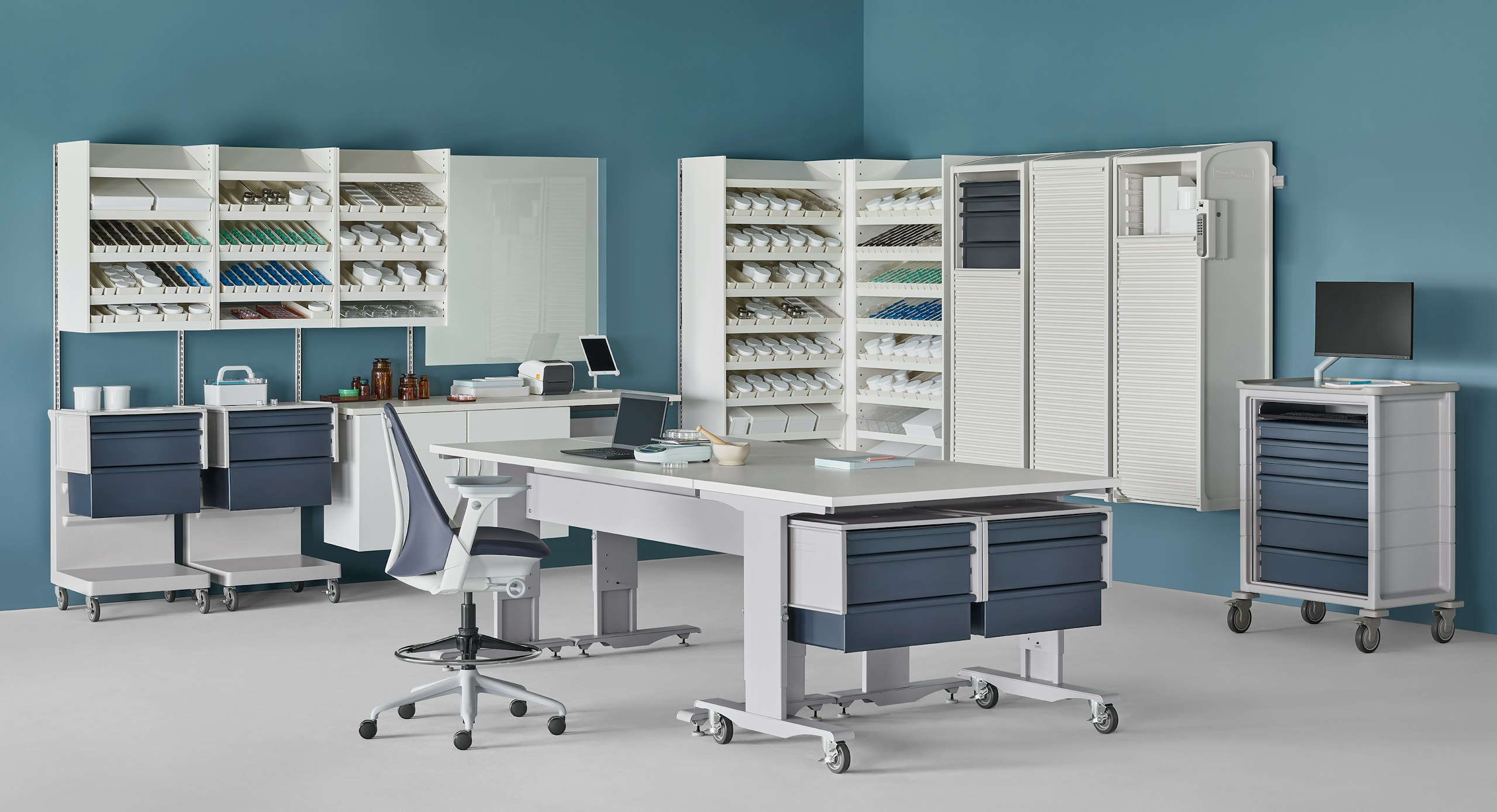 Pharmacy with white Co/Struc System of dispensing shelves, lockers, process tables, L Carts with blue drawers, a technology cart with blue drawers and a Sayl Stool.