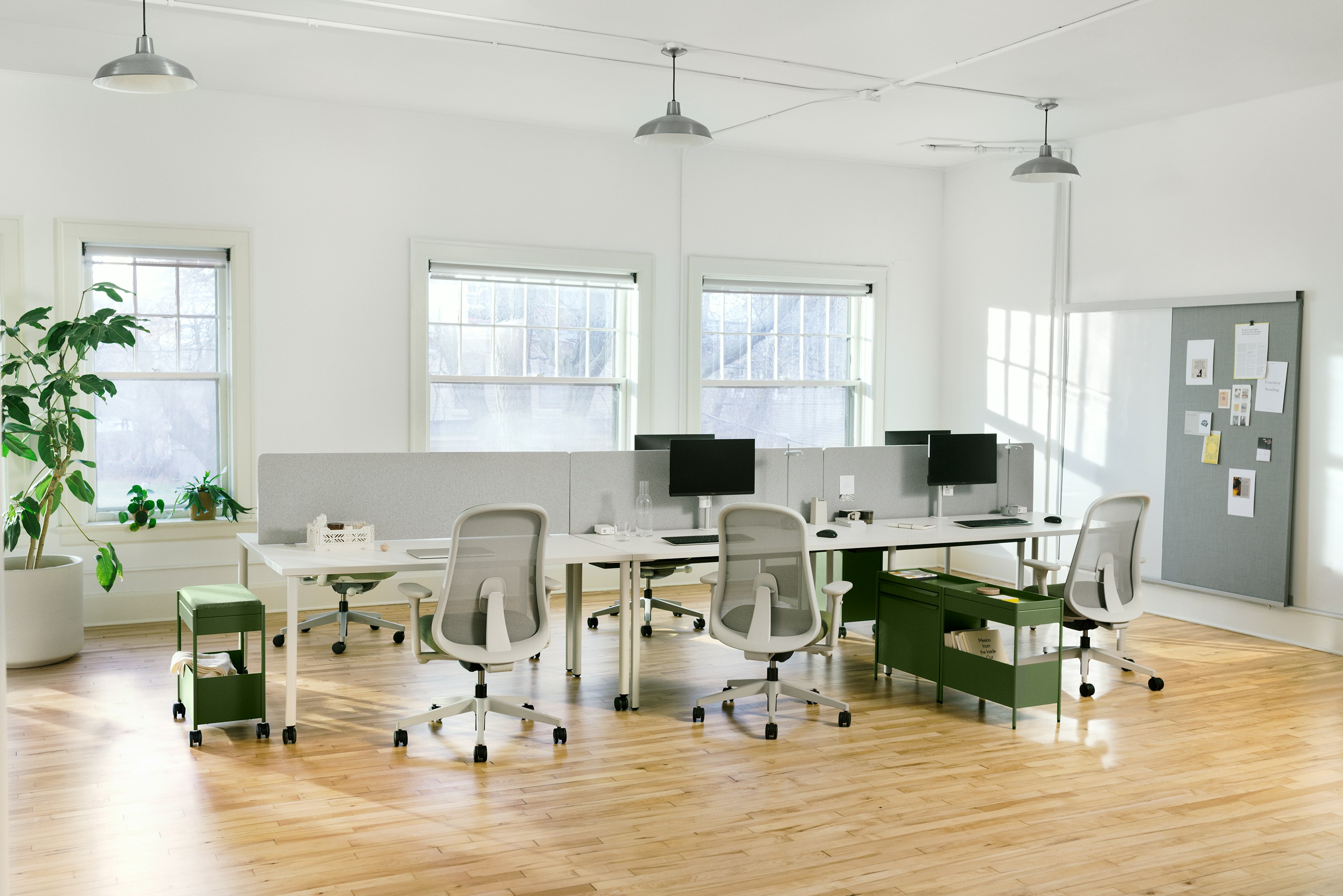 Four grey OE1 Rectangular Tables and a grey OE1 Project Table joined together to form a bench with green OE1 Storage Trolleys, green Lino Chairs and an OE1 Wall Rail and Board in the background.