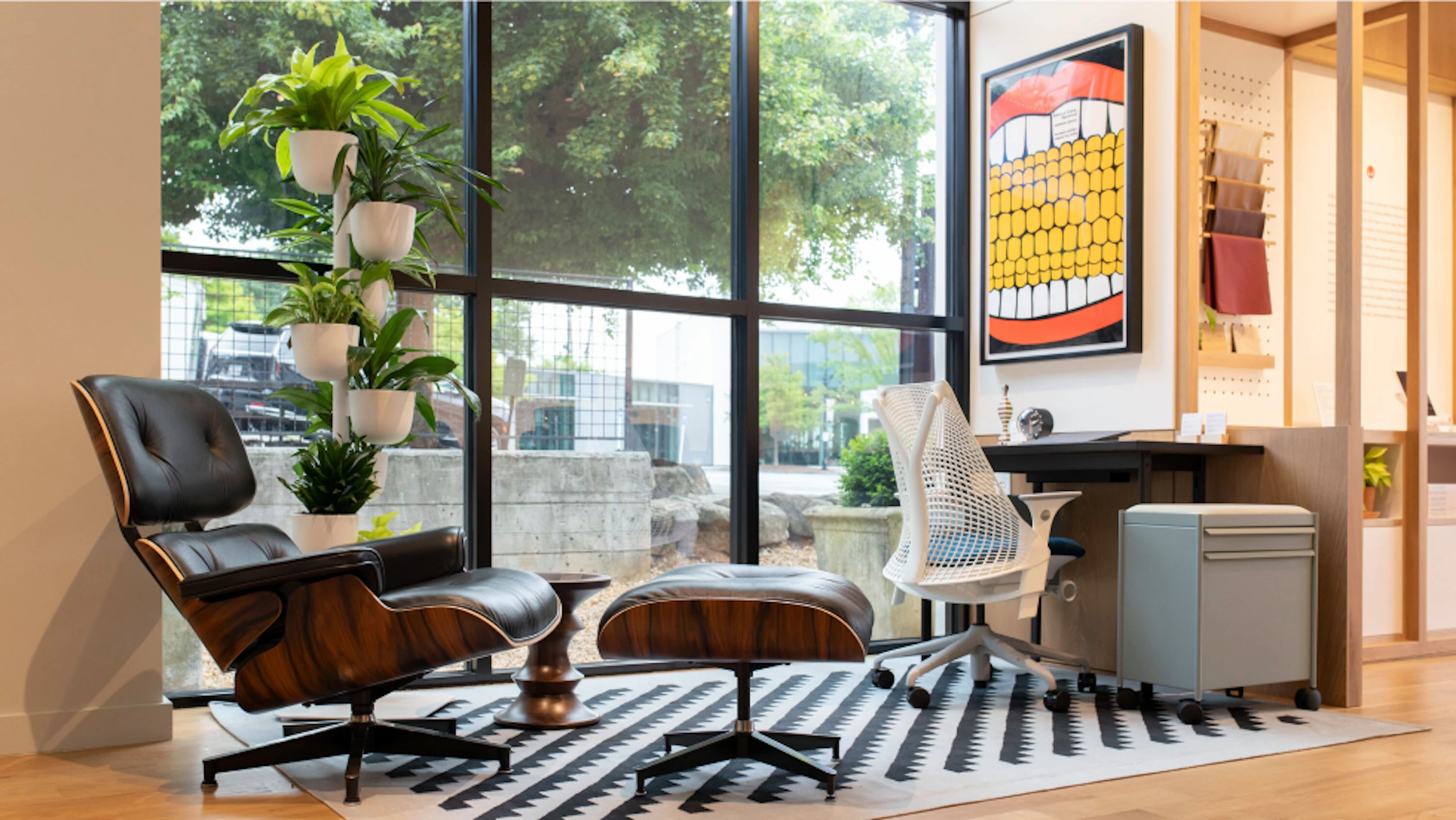 Several Herman Miller products, including an Eames Lounge Chair and Ottoman, Sayl Chair, and OE1 Storage Trolley, on a black and white rug at the Herman Miller Atlanta store