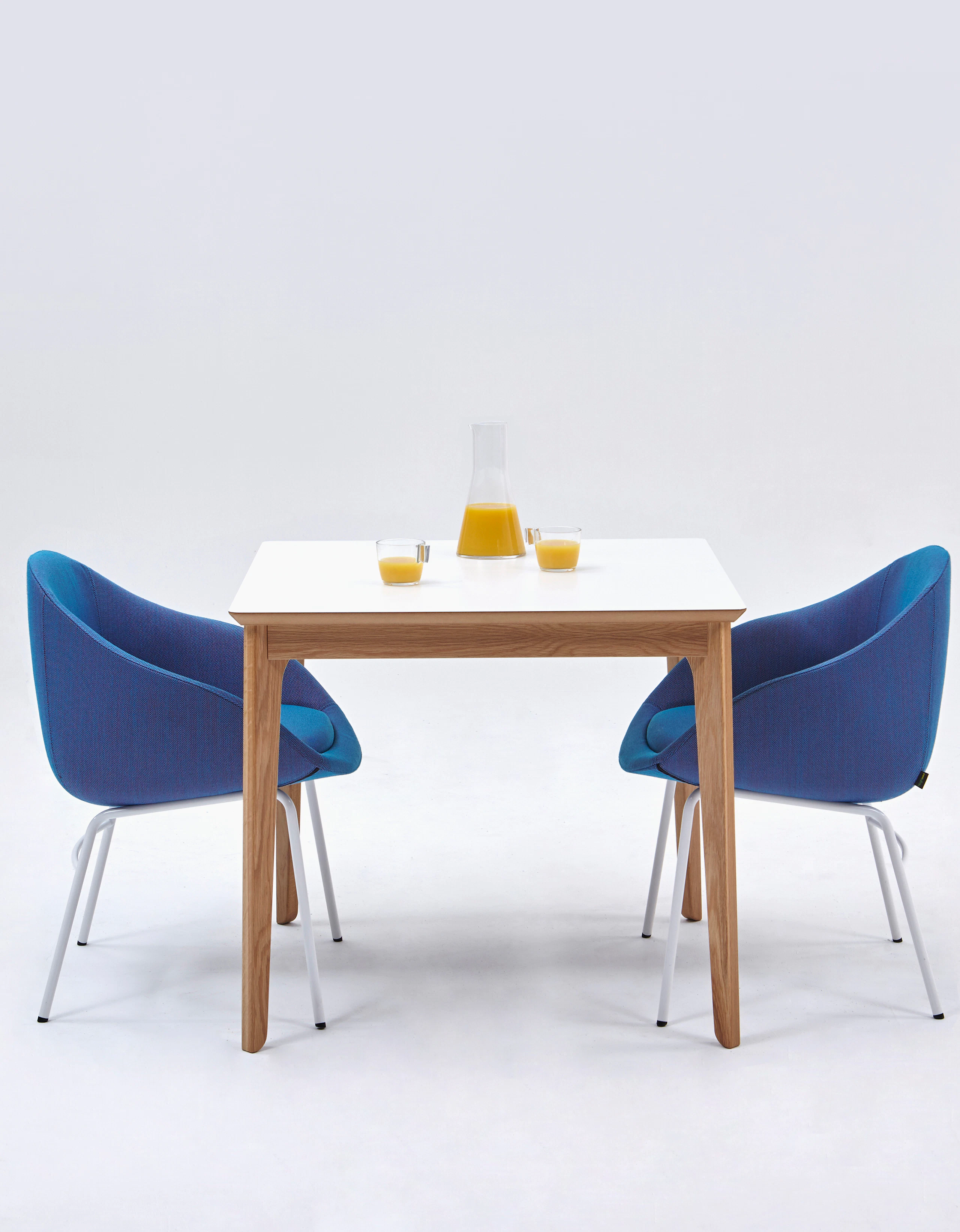 Two royal blue Always Side Chairs at a square white naughtone Dalby Café Table set with a carafe and two half-full glasses of orange juice.