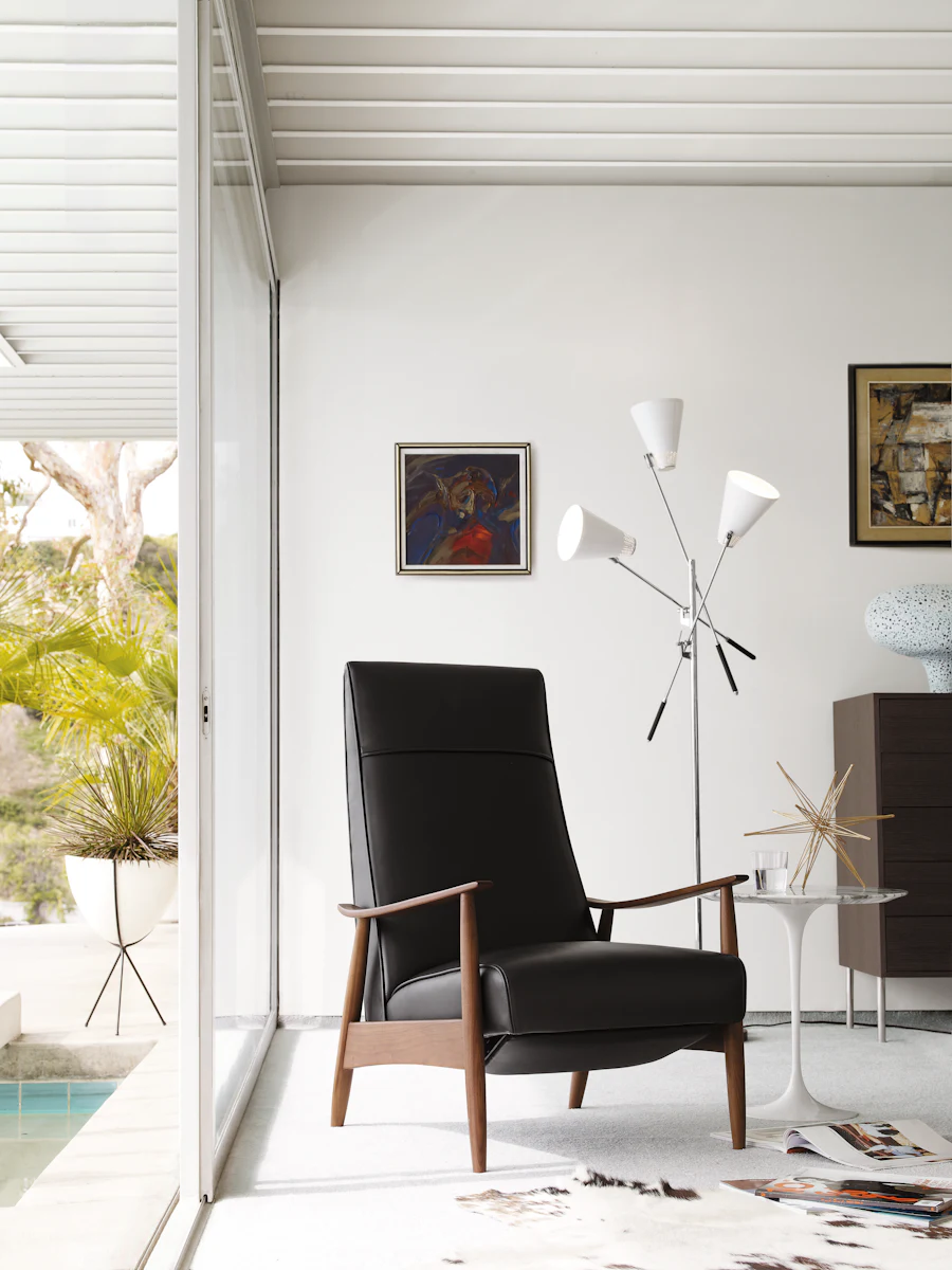Minimalist chair with black leather and wooden legs in a bright room with a round marble top side table.