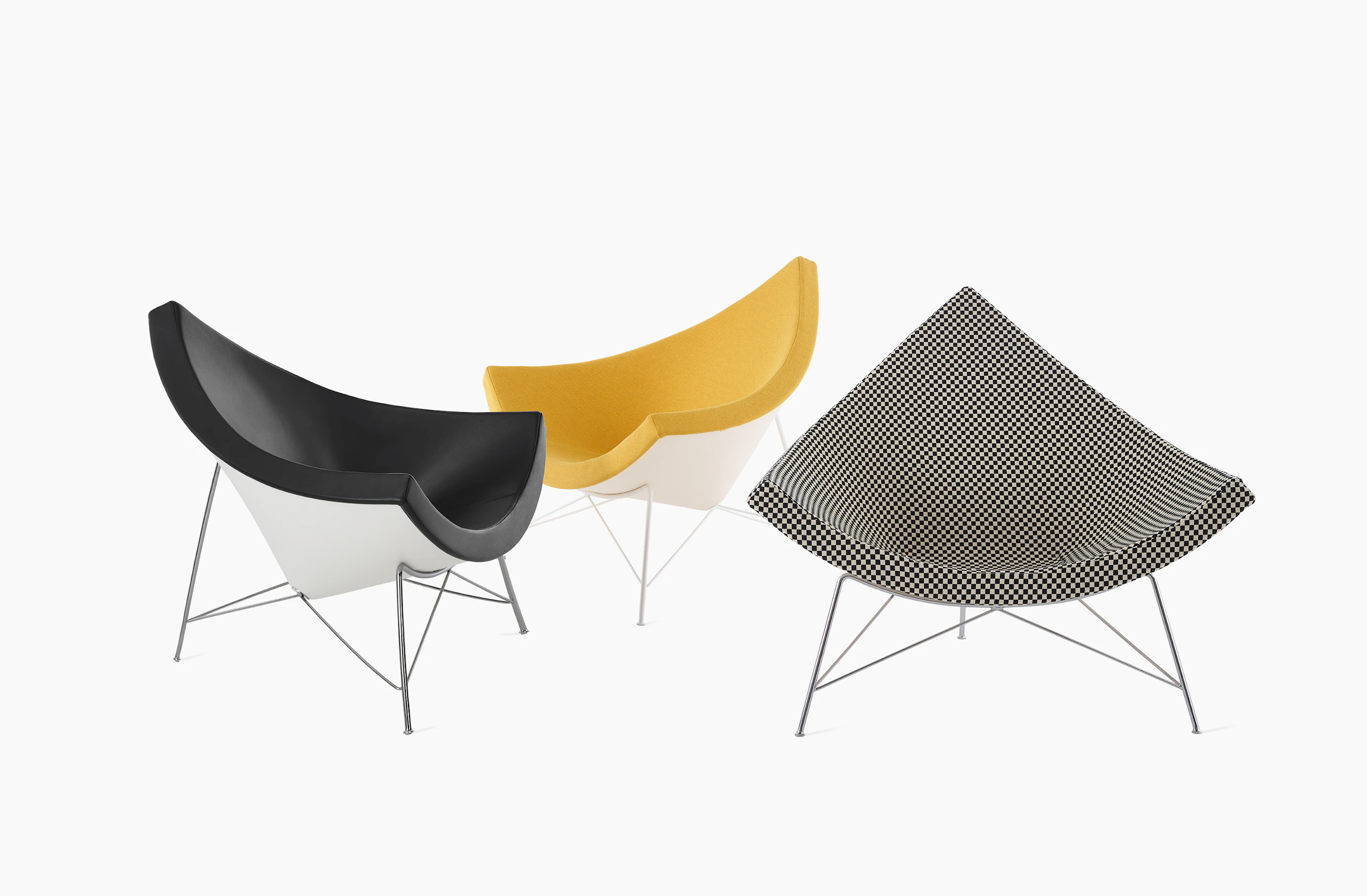 Three Nelson Coconut Lounge chairs arranged in different angles. A dark grey chair faces a yellow chair in opposing 45-degree angles and a black and white checkerboard chair is placed to the right of them facing forward.