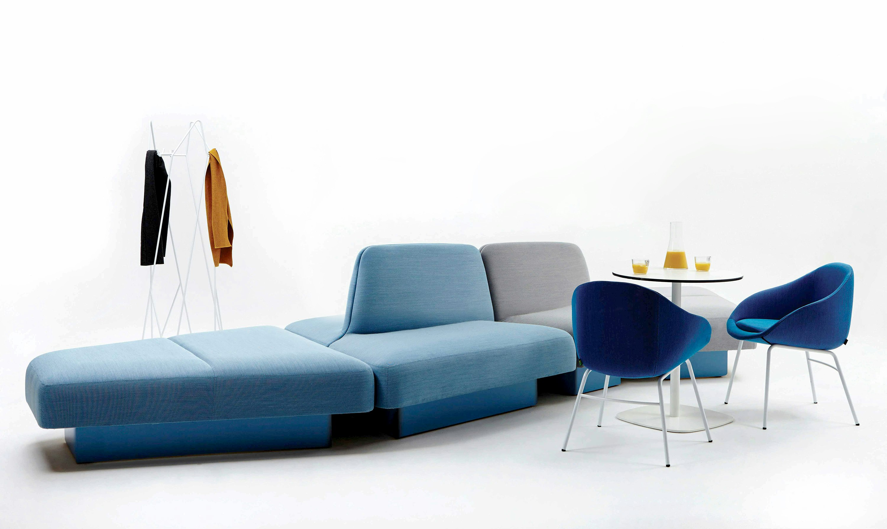 White sweep view of large modular sofa with chairs, table and coat stand.