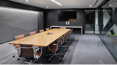 A large conference room with grey carpet and walls furnished with a large conference table, mounted TV screen, and brown Herman Miller Eames Aluminum Group Chairs