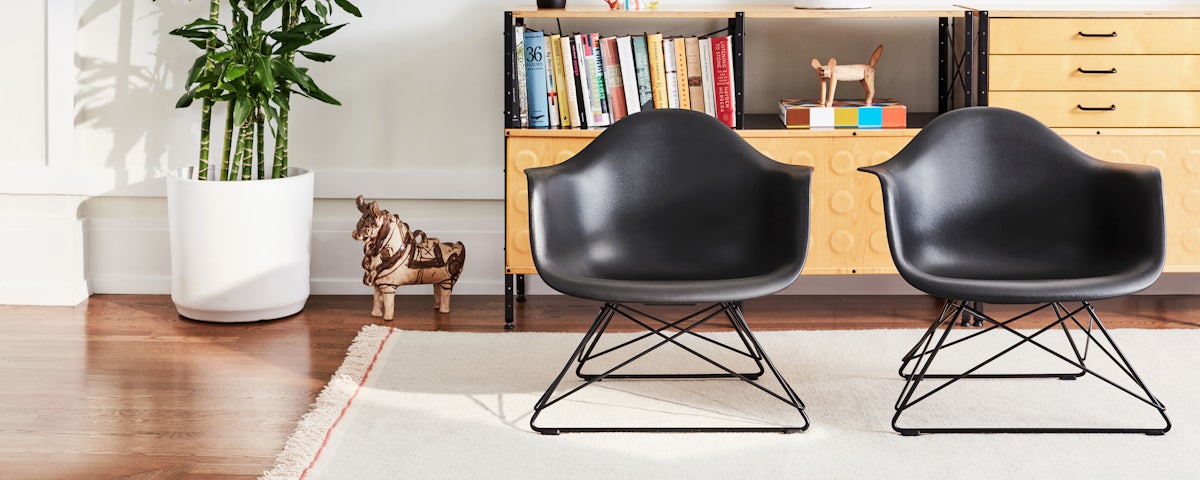 Two Eames Molded Plastic Armchairs with low wire bases on a rug in a living room setting.