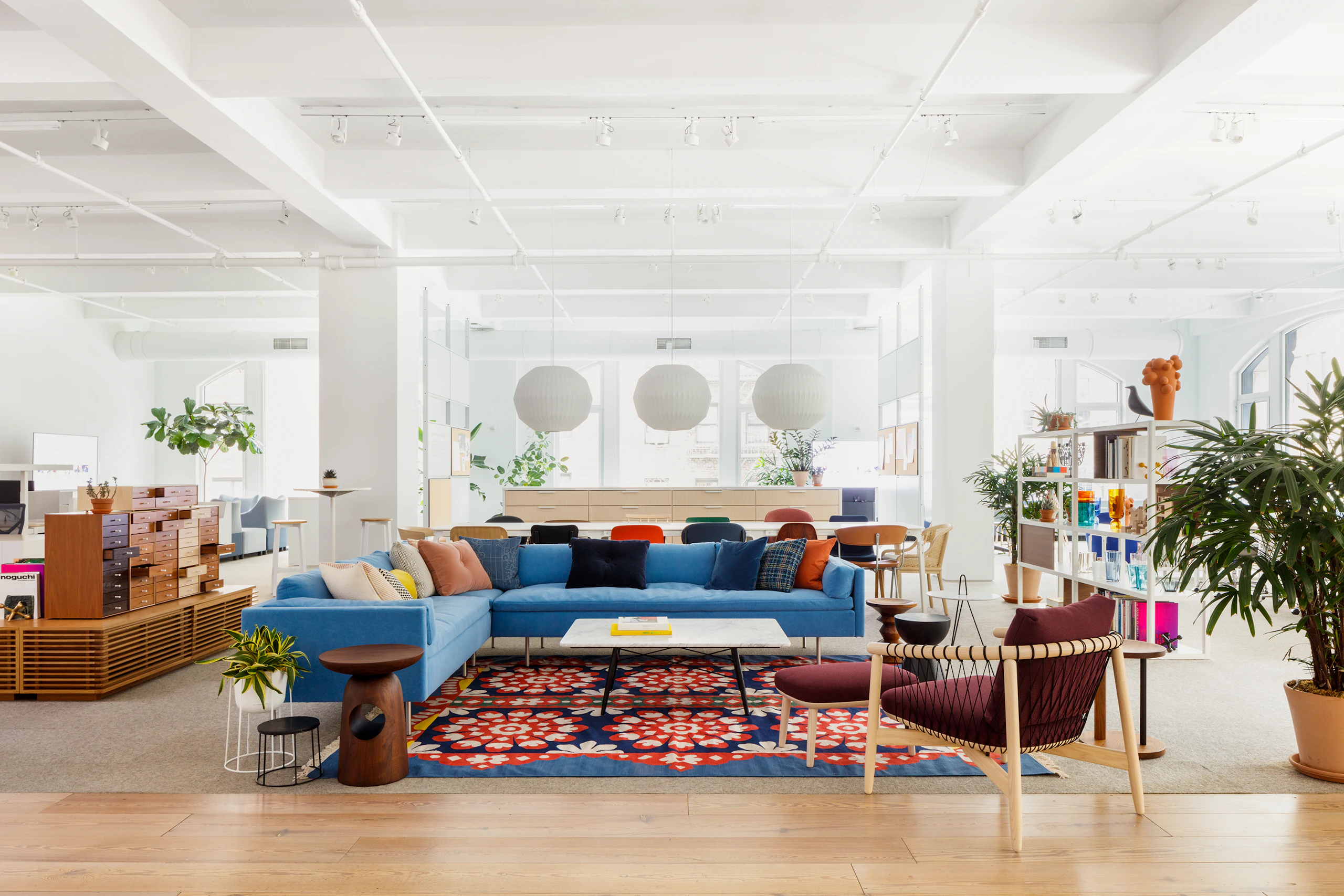Environmental shot of blue Bolster Sofa, white Eames Coffee table, and burgundy Crosshatch side chair with light brown frame.
