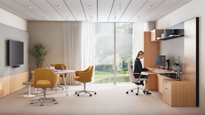 A person working at a computer in a private office setting furnished with Geiger Taper Chairs, a Knoll Grasshopper Table, Saarinen Executive Chairs, and Saarinen Tulip Stools.