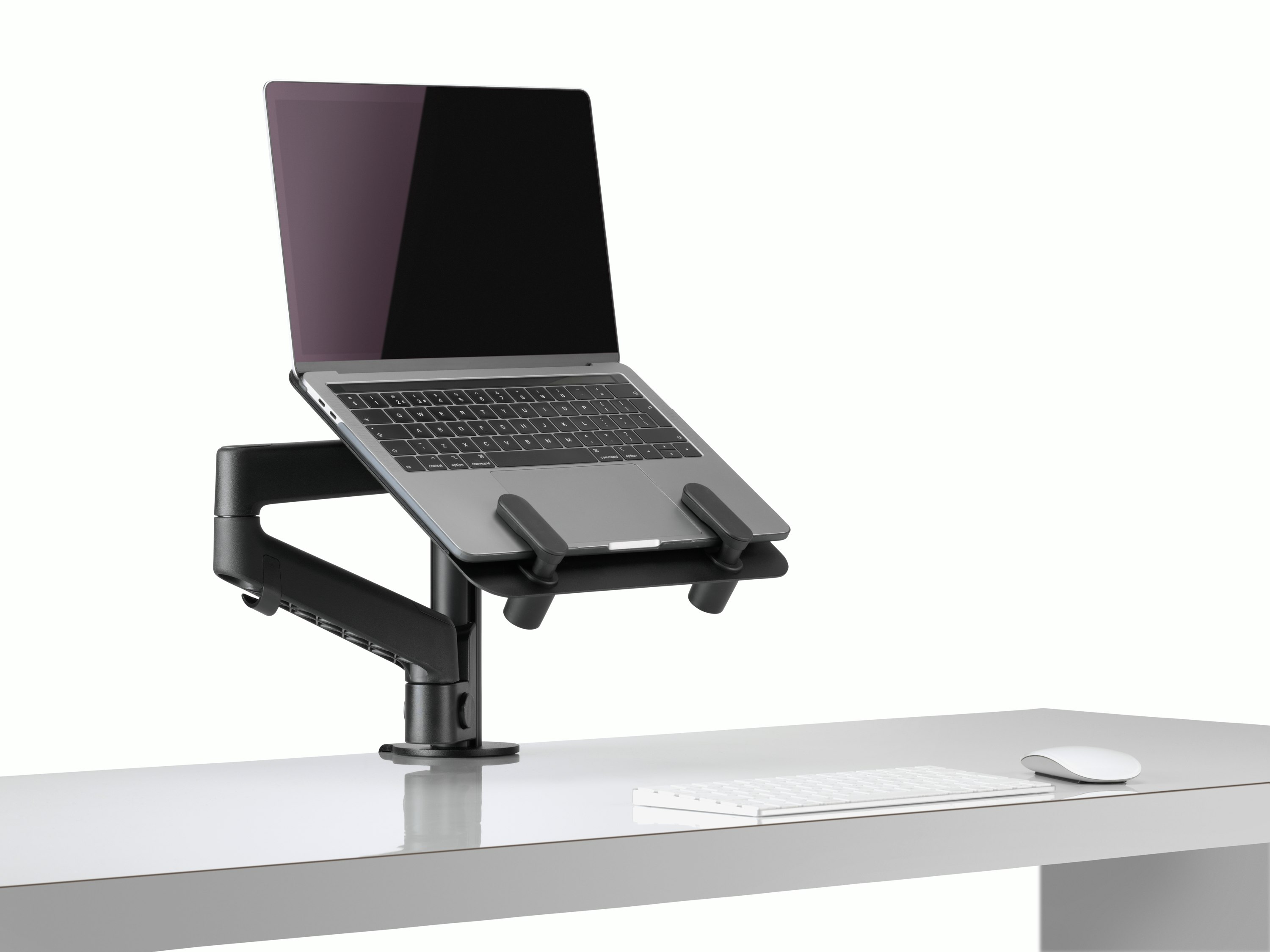 Side angle view of an open laptop raised from a desk and supported by a black Lima Laptop Mount and Lima Monitor Arm.