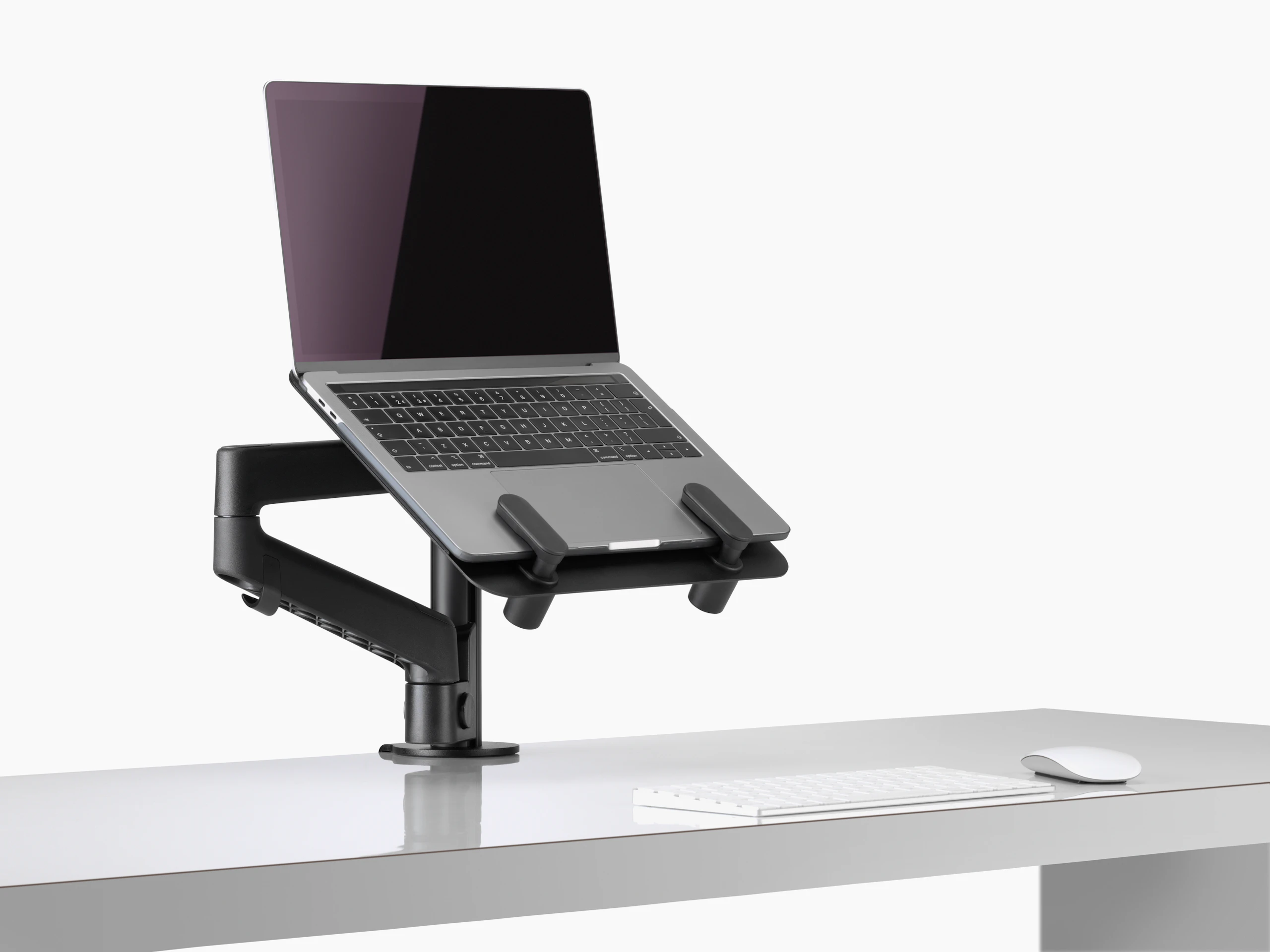 Side angle view of an open laptop raised from a desk and supported by a black Lima Laptop Mount and Lima Monitor Arm.
