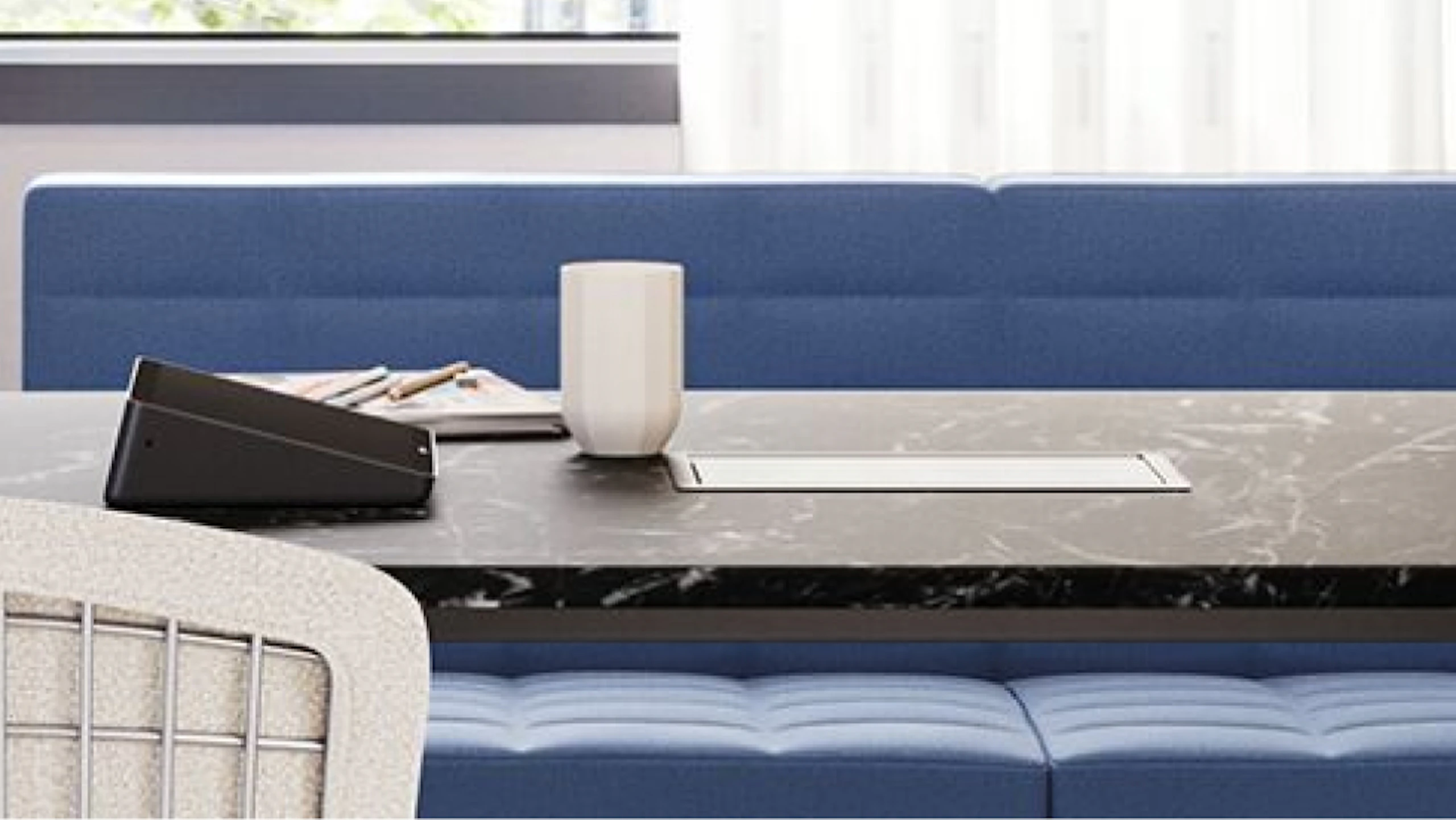 A coffee mug and assorted work papers atop a black and white Knoll Grasshopper table that features a blue Geiger Tuxedo Component Lounge and white Knoll Bertoia chair in a group conference room setting designed to facilitate employee connection.