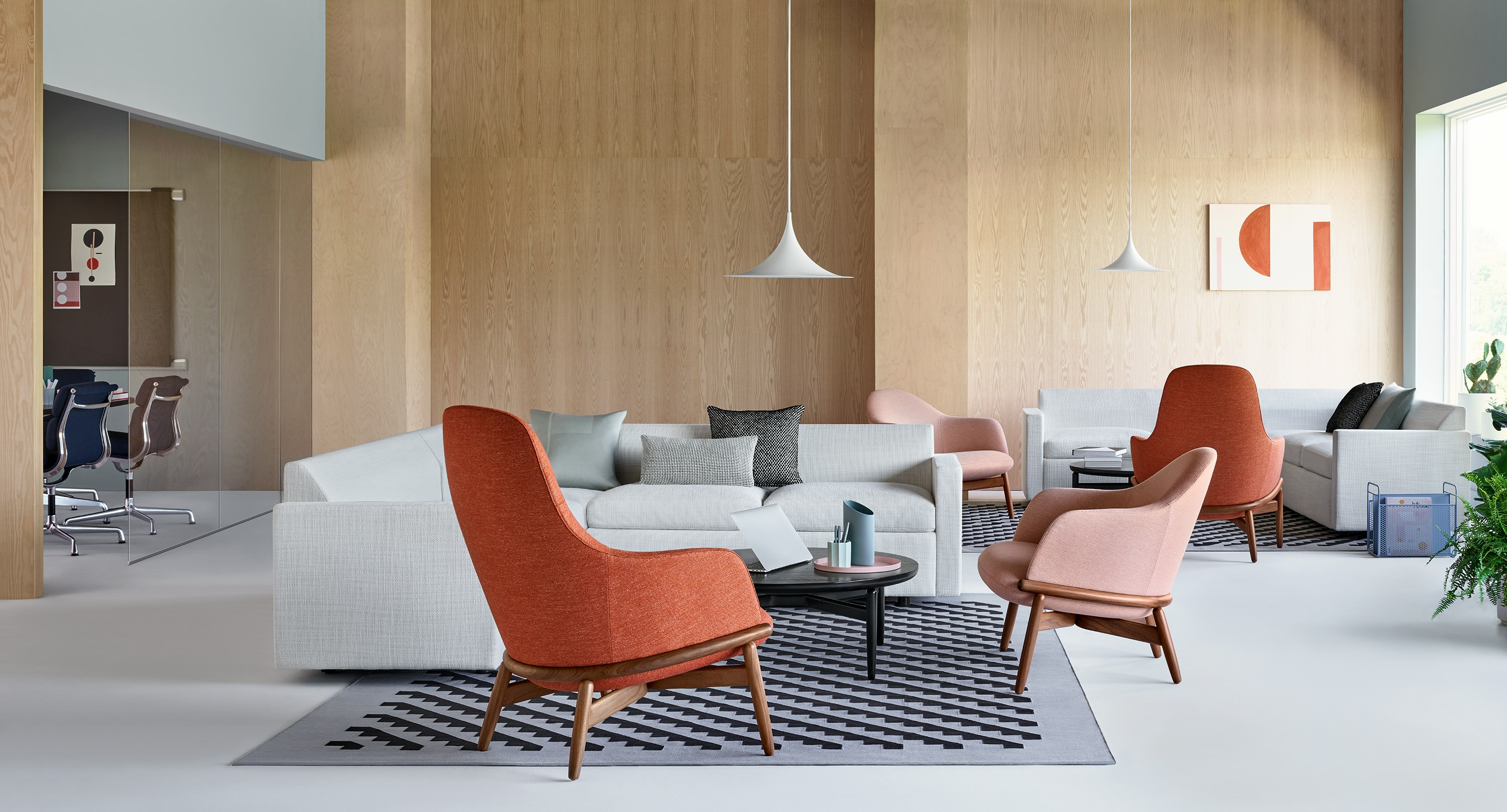 A relaxed lounge setting with Reframe Lounge Chairs in the foreground. A Bevel Sofa sits on a patterned rug in the background.