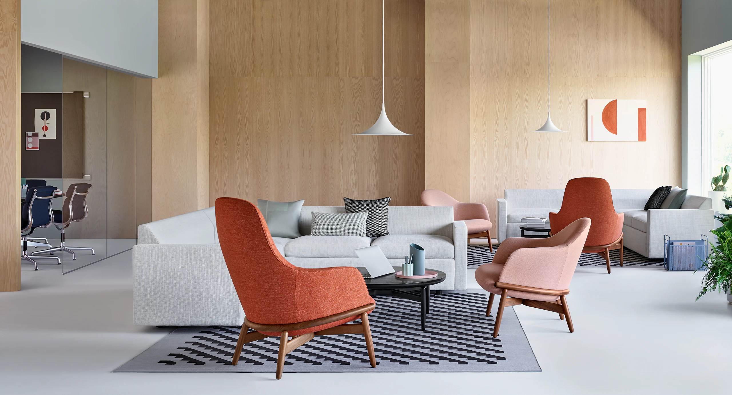 A relaxed lounge setting with Reframe Lounge Chairs in the foreground. A Bevel Sofa sits on a patterned rug in the background.