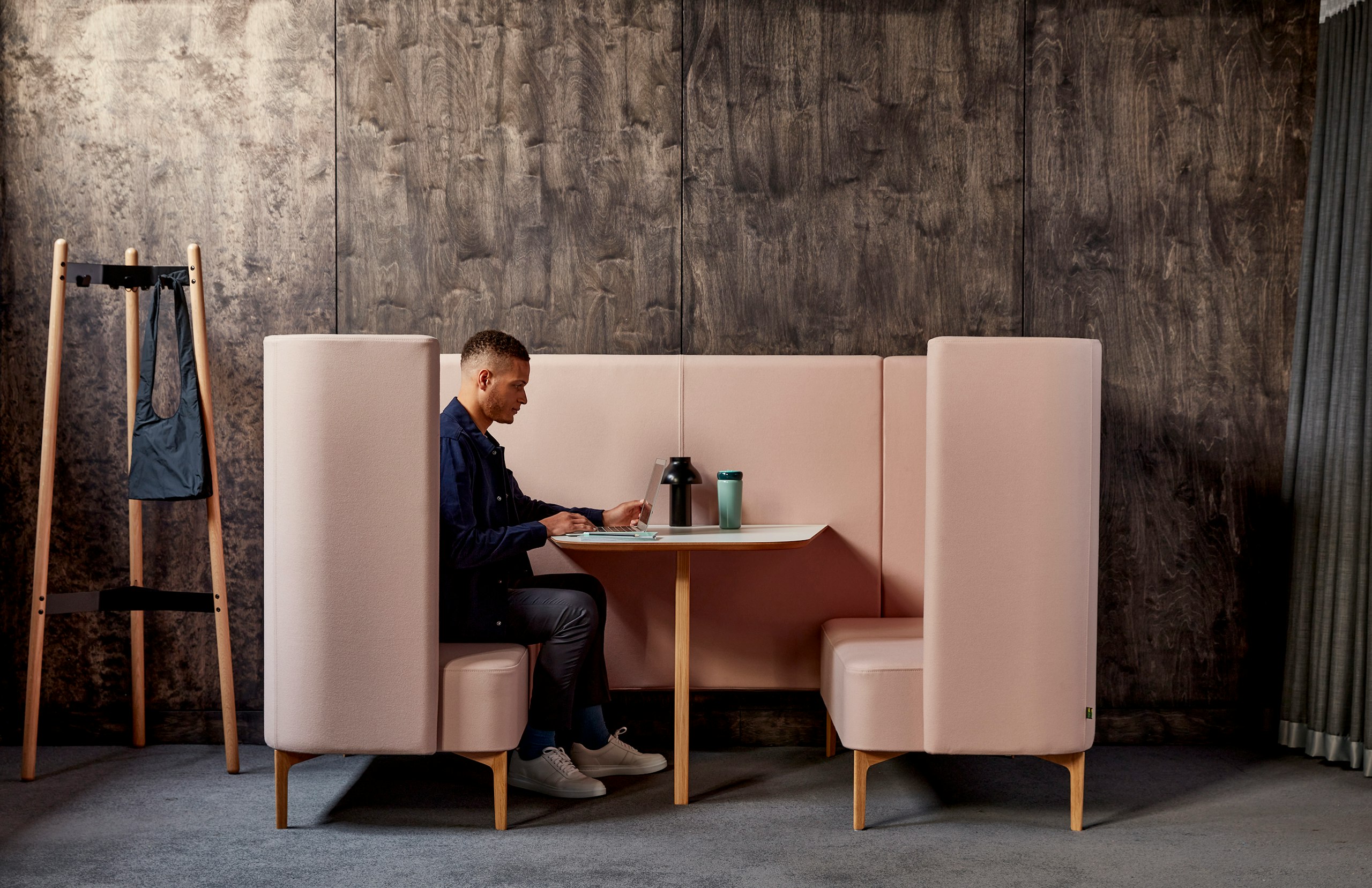 Man sitting within pale pink Pullman booth with white table top and oak legs.