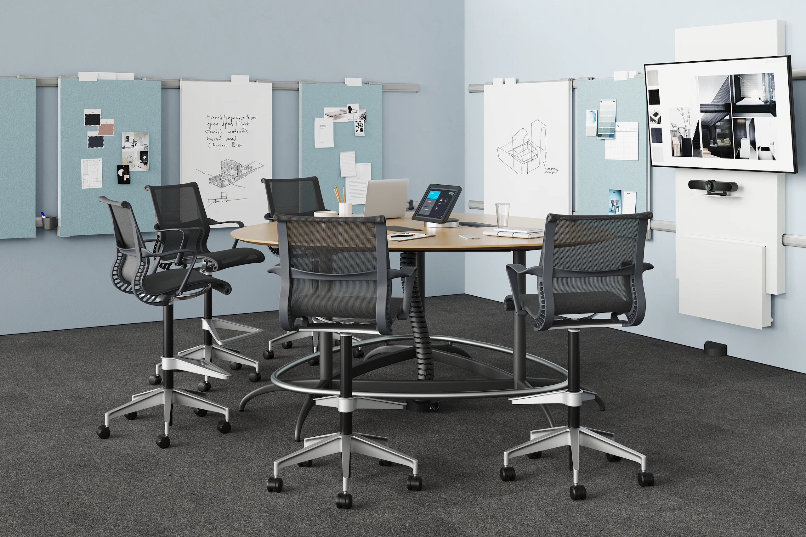 A meeting room setting featuring an Exclave table with five black Setu Stools in front of a monitor and Exclave display elements.