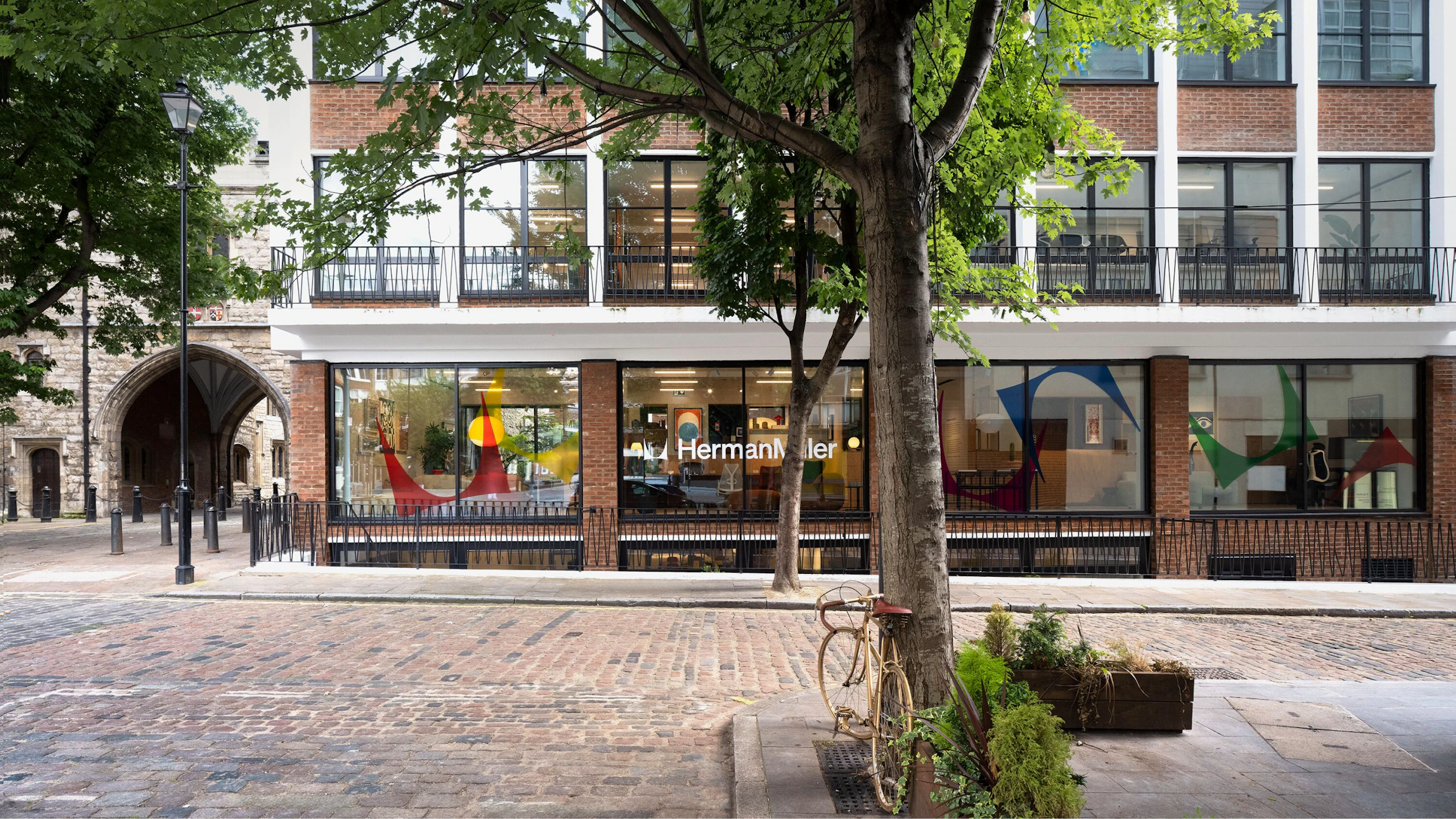 Several green trees on a brick-laden street outside of the MillerKnoll London showroom at The Sans building