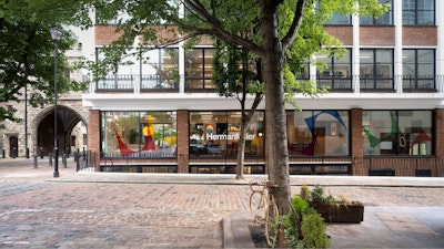 Several green trees on a brick-laden street outside of the MillerKnoll London showroom at The Sans building