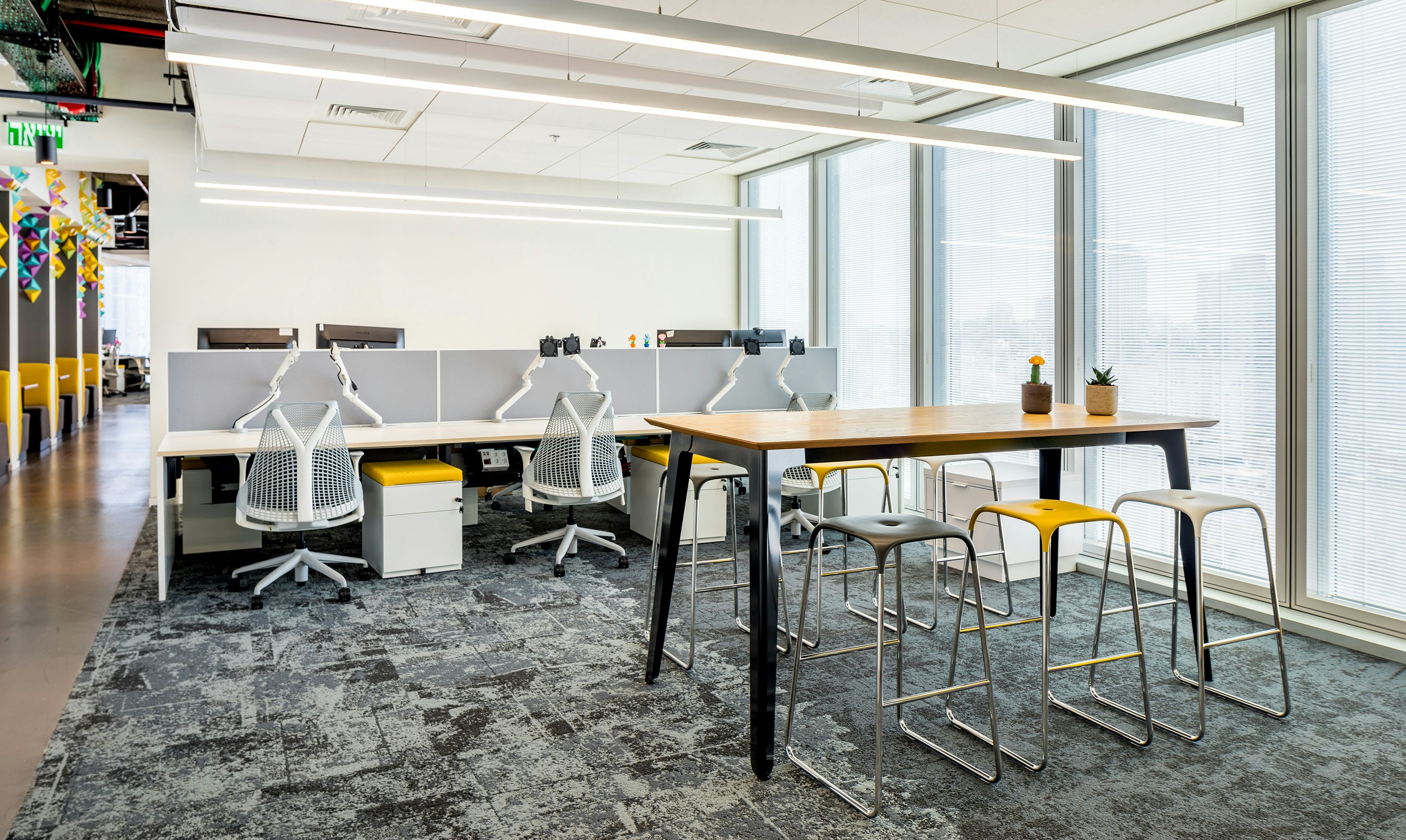 A black naughtone Fold Bar Height Table and stools in a high-rise office, a benching system and Sayl Chairs by Herman Miller in the background.