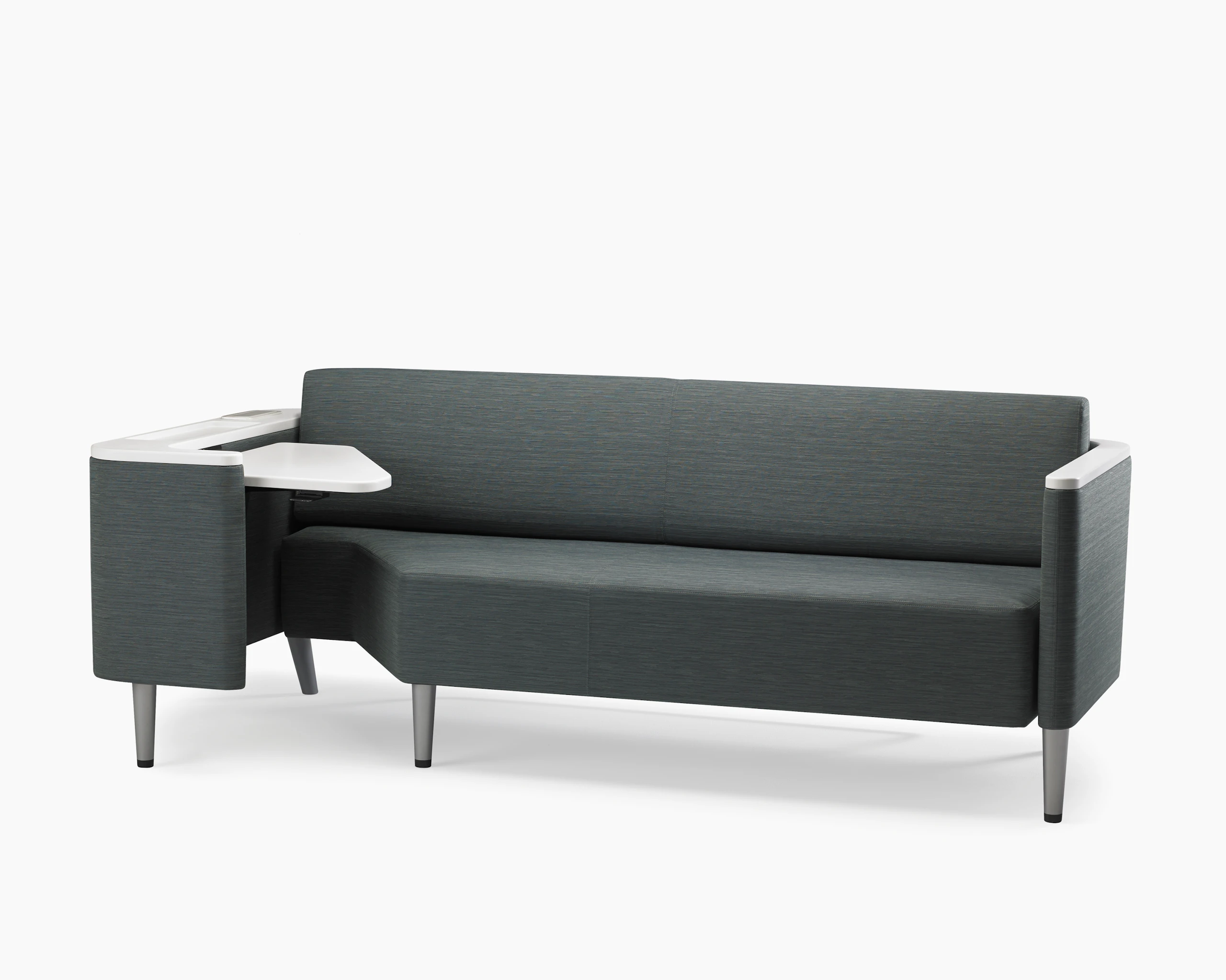 A Palisade Flop sofa in dark grey textile with white solid surface arms caps and white adjustable table with Durawrap top.