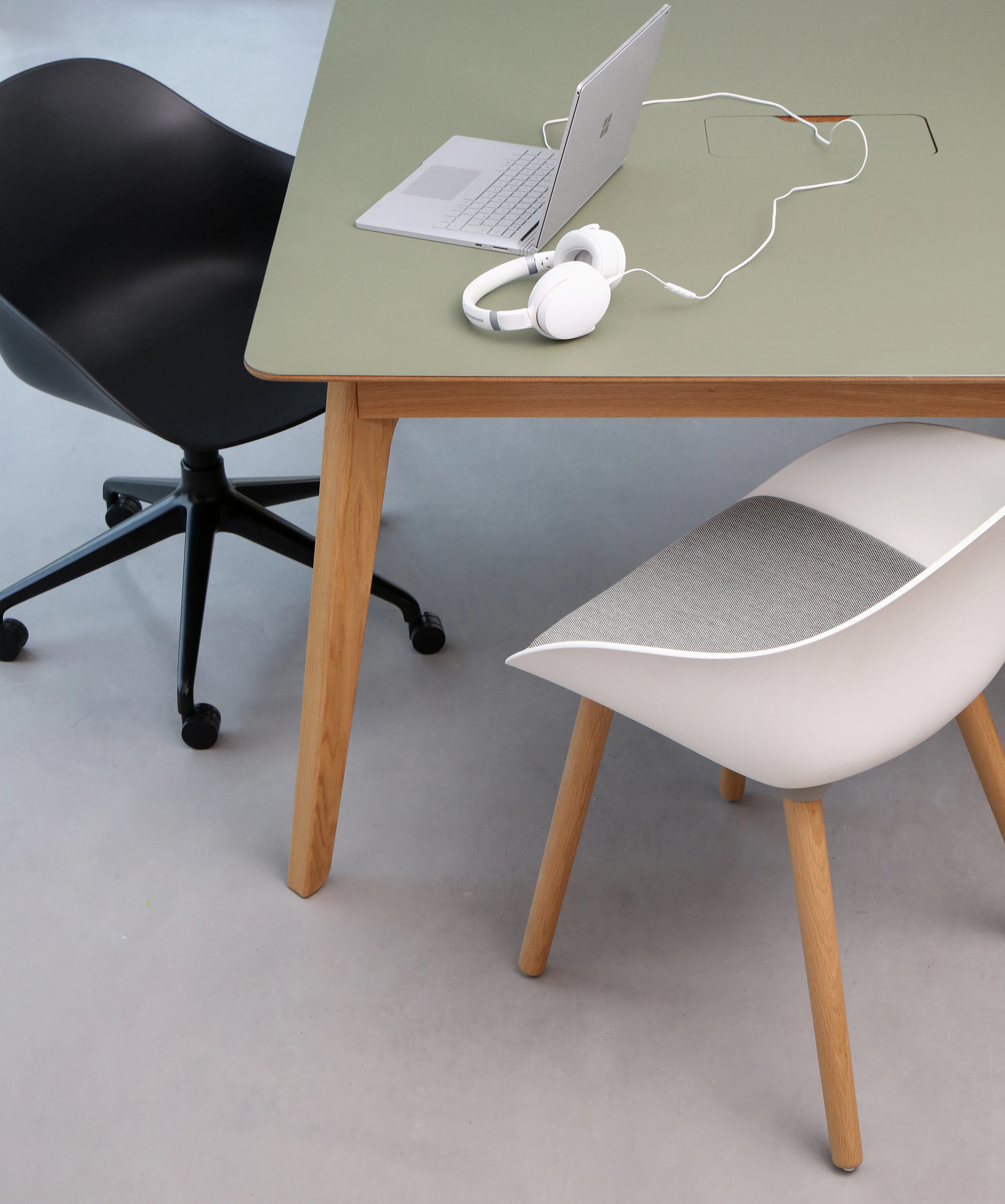 A black Ruby Chair with matching 5-star base with casters, next to a white Ruby chair on oak dowel base and a table.