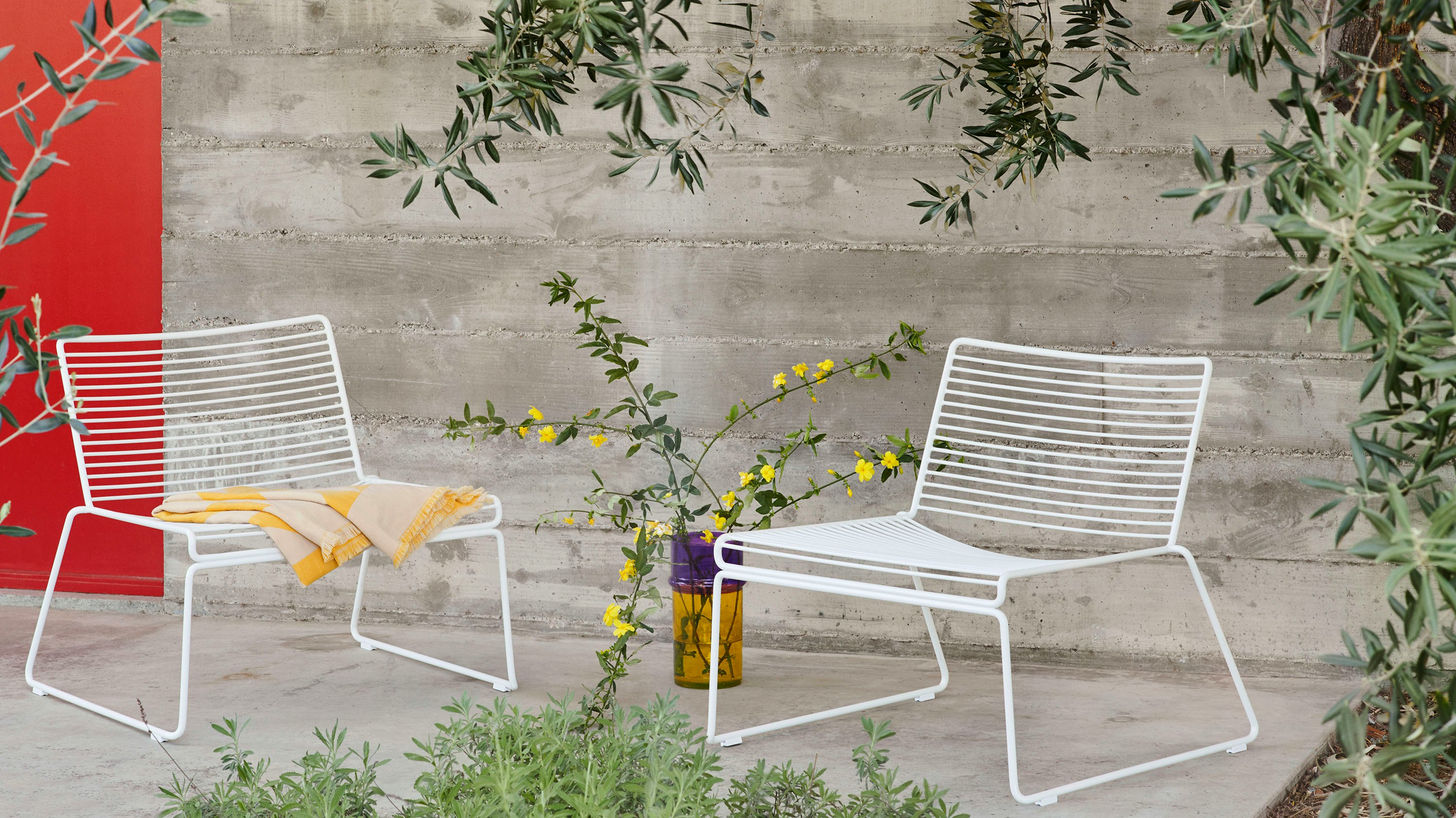 Two white Hee Lounge Chairs in a courtyard.
