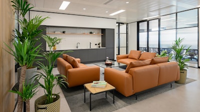 A communal seating area furnished with three leather Outline Sofas by Muuto, a clear-glass coffee table, and potted plants