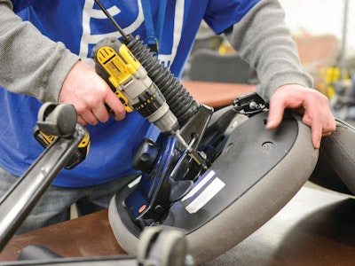 A close up view of a person holding the bottom, underside, section of an office chair and using a drill to secure parts during assembly.