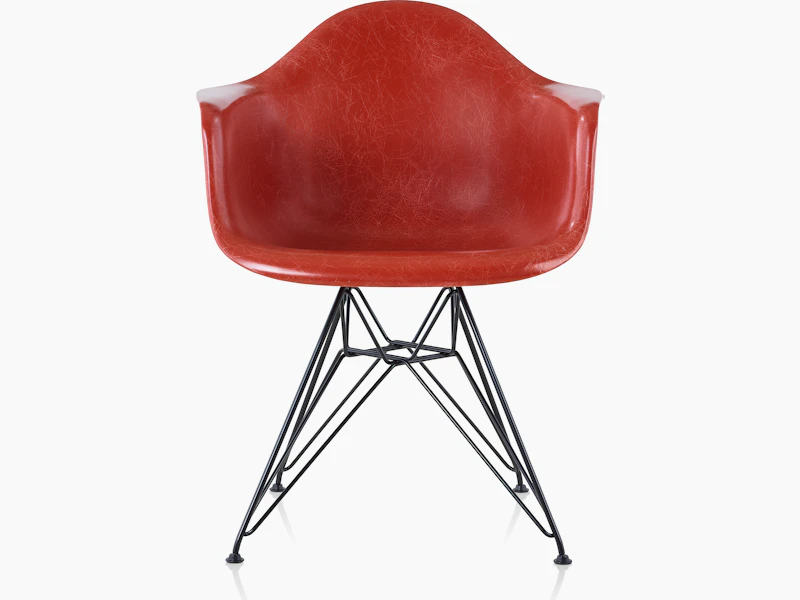 A red Eames Molded Fiberglass Chair with arms and a wire base, viewed from the front.