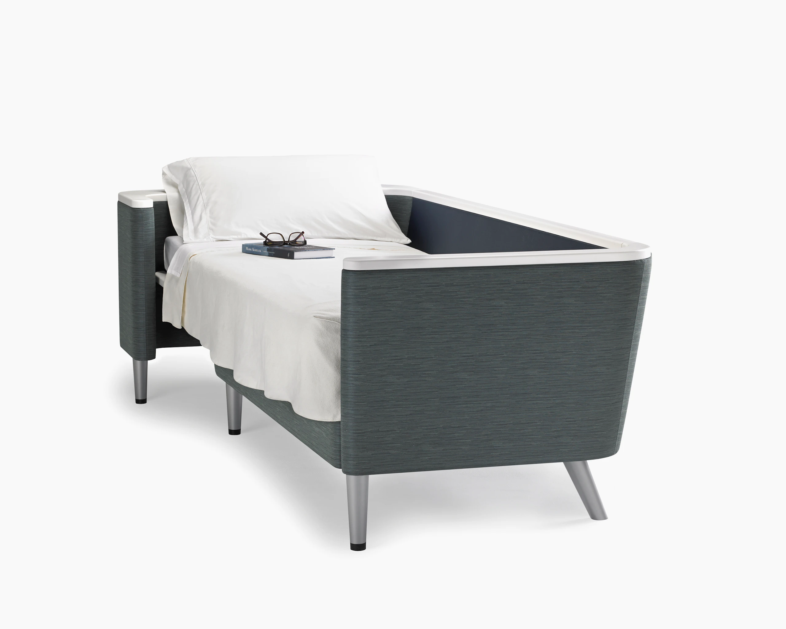 A Palisade Flop sofa converted to sleep surface in dark grey textile with white solid surface arms caps and white pillow and sheet.