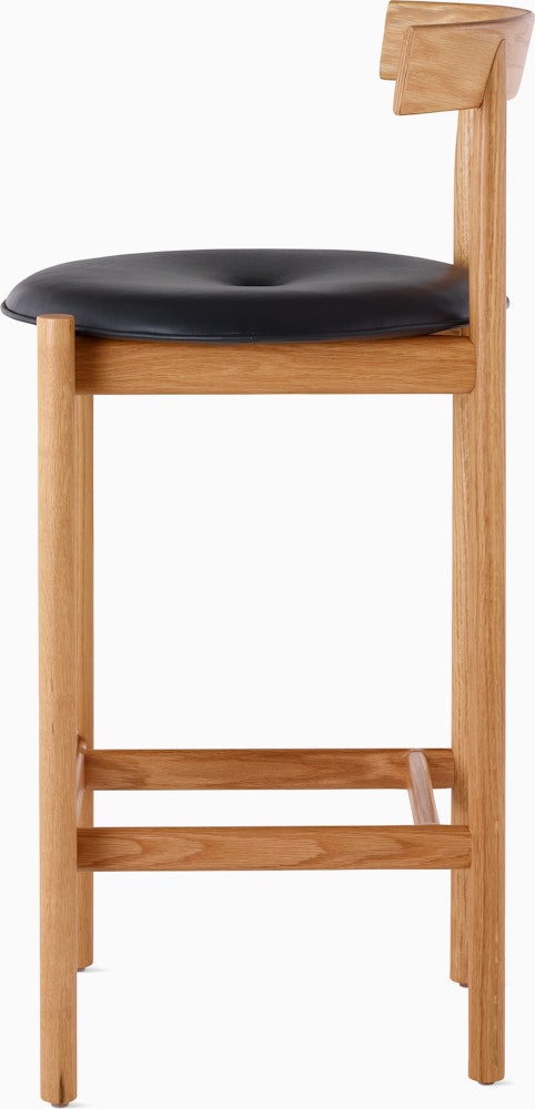 Profile view of an oak Comma Stool with a seat pad.