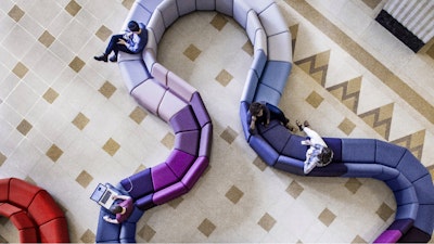 An aerial view of a winding sectional sofa featuring several different shades of blue, purple, and red at The Sans building in London
