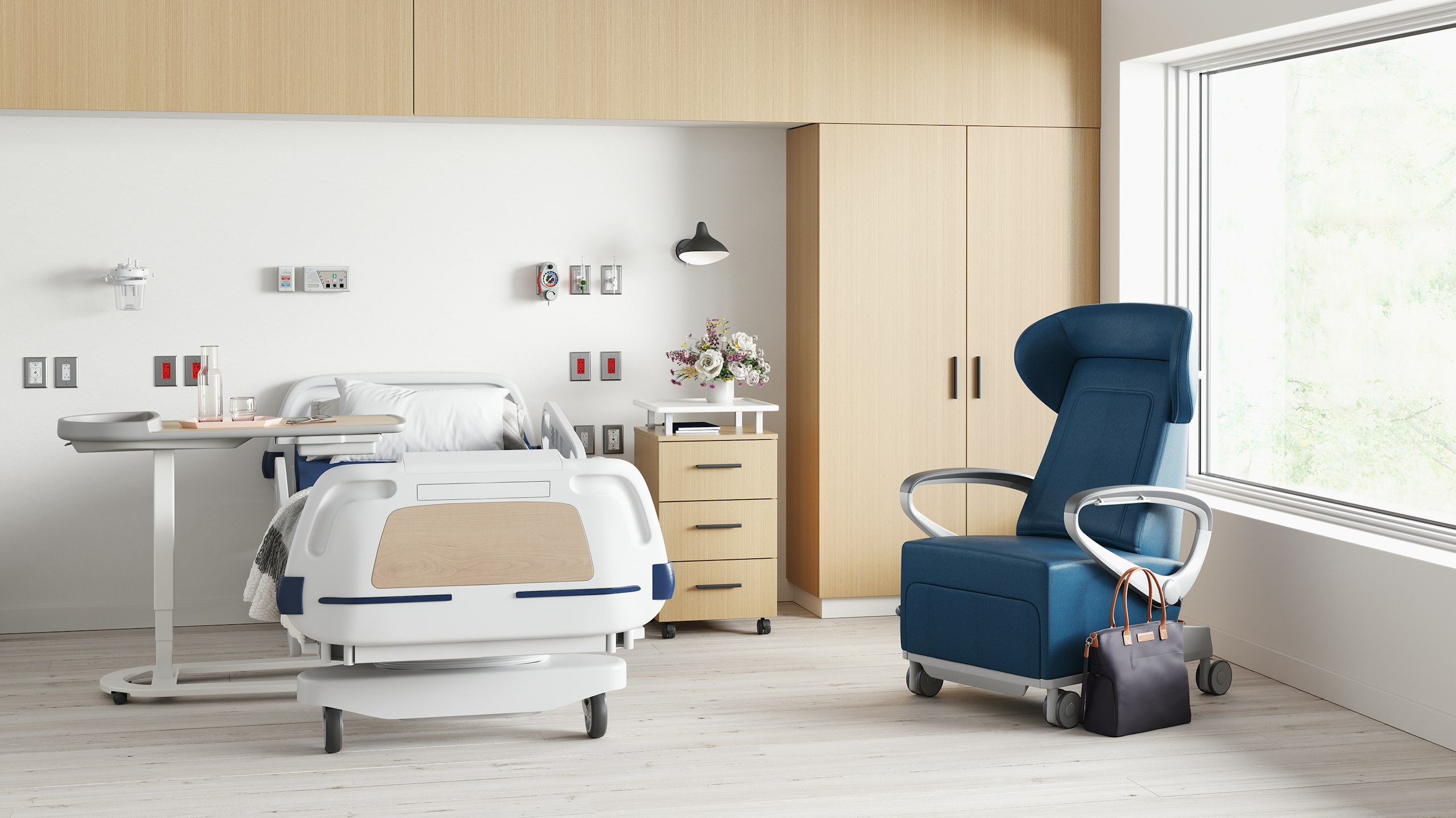 A patient room with the Mirage Overbed Table placed by a hospital bed. A Nemschoff Bedside Cabinet and a Mora wardrobe both in an ash finish next to it, and a Nemschoff Ava Recliner in a blue upholstery nearby.