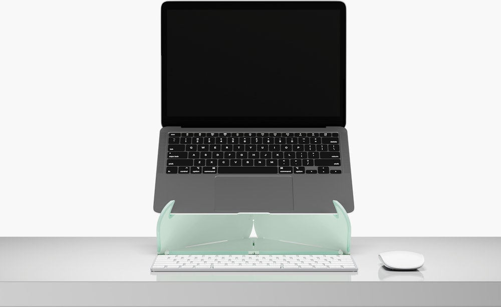 An open laptop raised to eye level on an Oripura Laptop Stand In mint green placed on a desk with work tools.