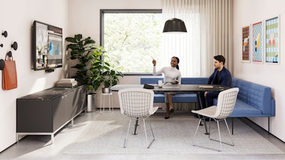 A group setting featuring two people sitting on a blue corner bench while participating in a virtual meeting in a conference room furnished with Geiger Tuxedo Component Lounge seating, a Knoll Grasshopper Table, and a Knoll Florence Knoll Credenza