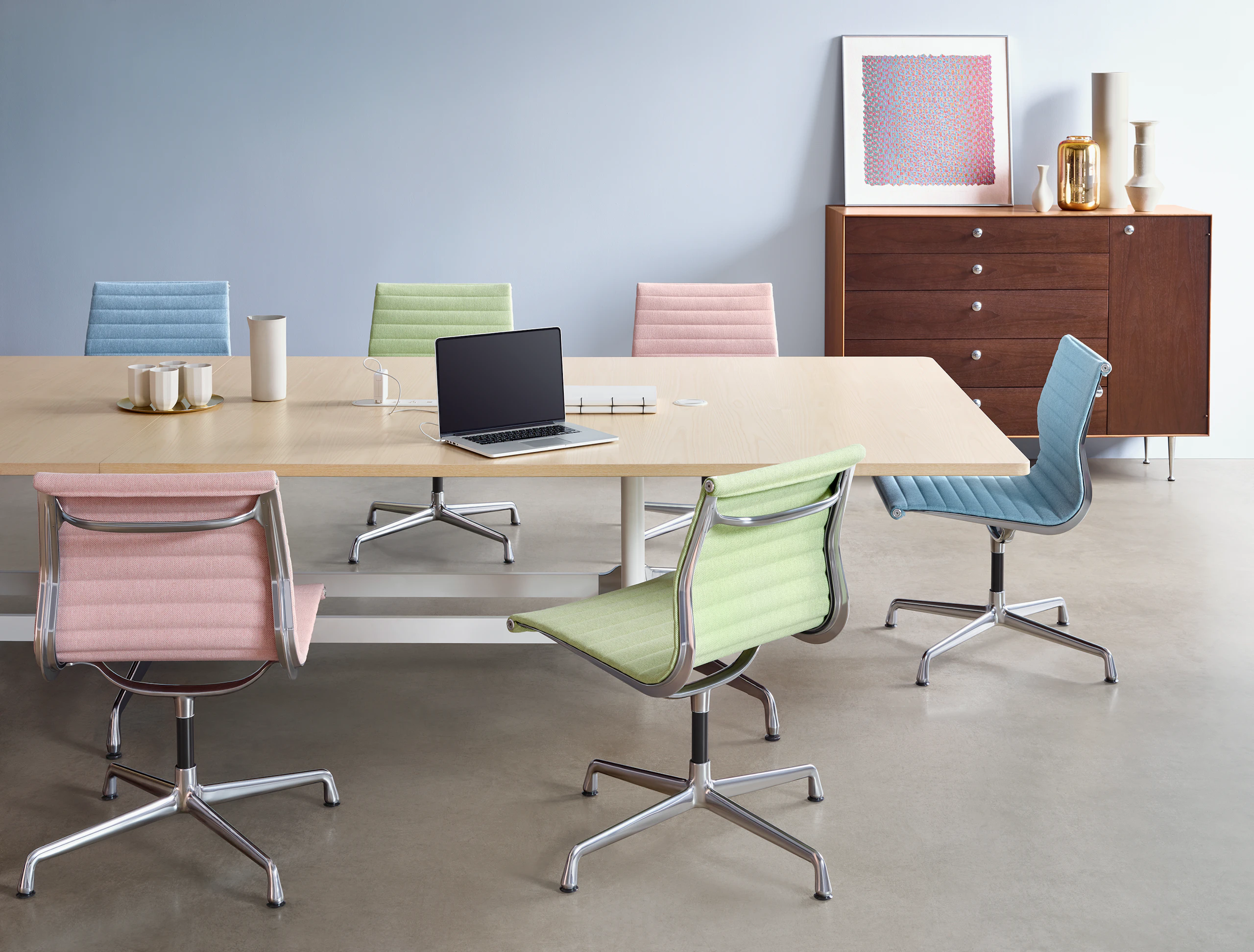 A group of colorful Eames Aluminum Group Side Chairs arranged around a large Eames Table in a Meeting Space.