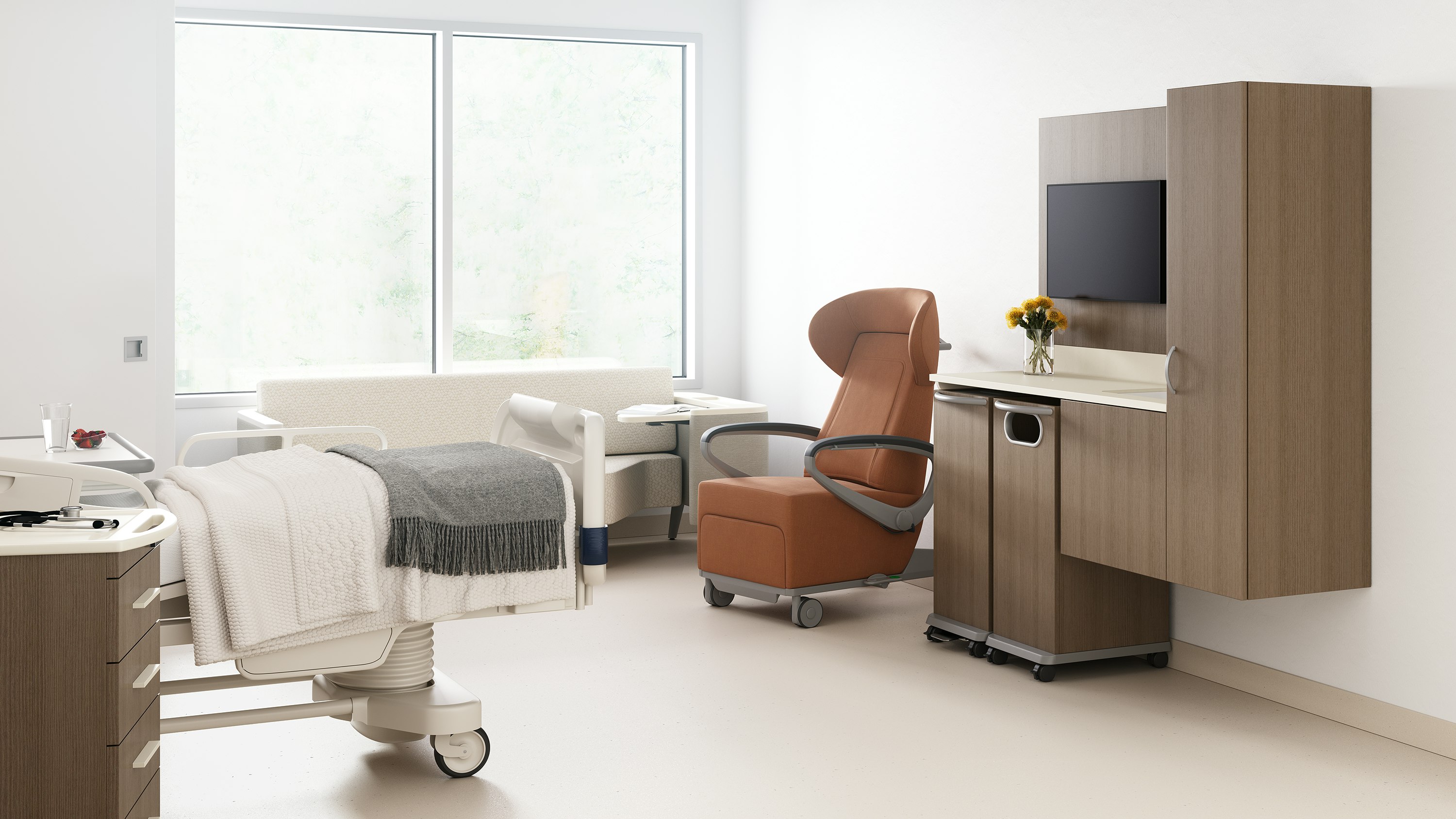 A patient room with a footwall of Mora casework with a trash cart and linen cart in medium brown wood finish, an Ava recliner in tan, a Palisade Flop Sofa in off white, a patient bed, with a Mora supply cart next to it.