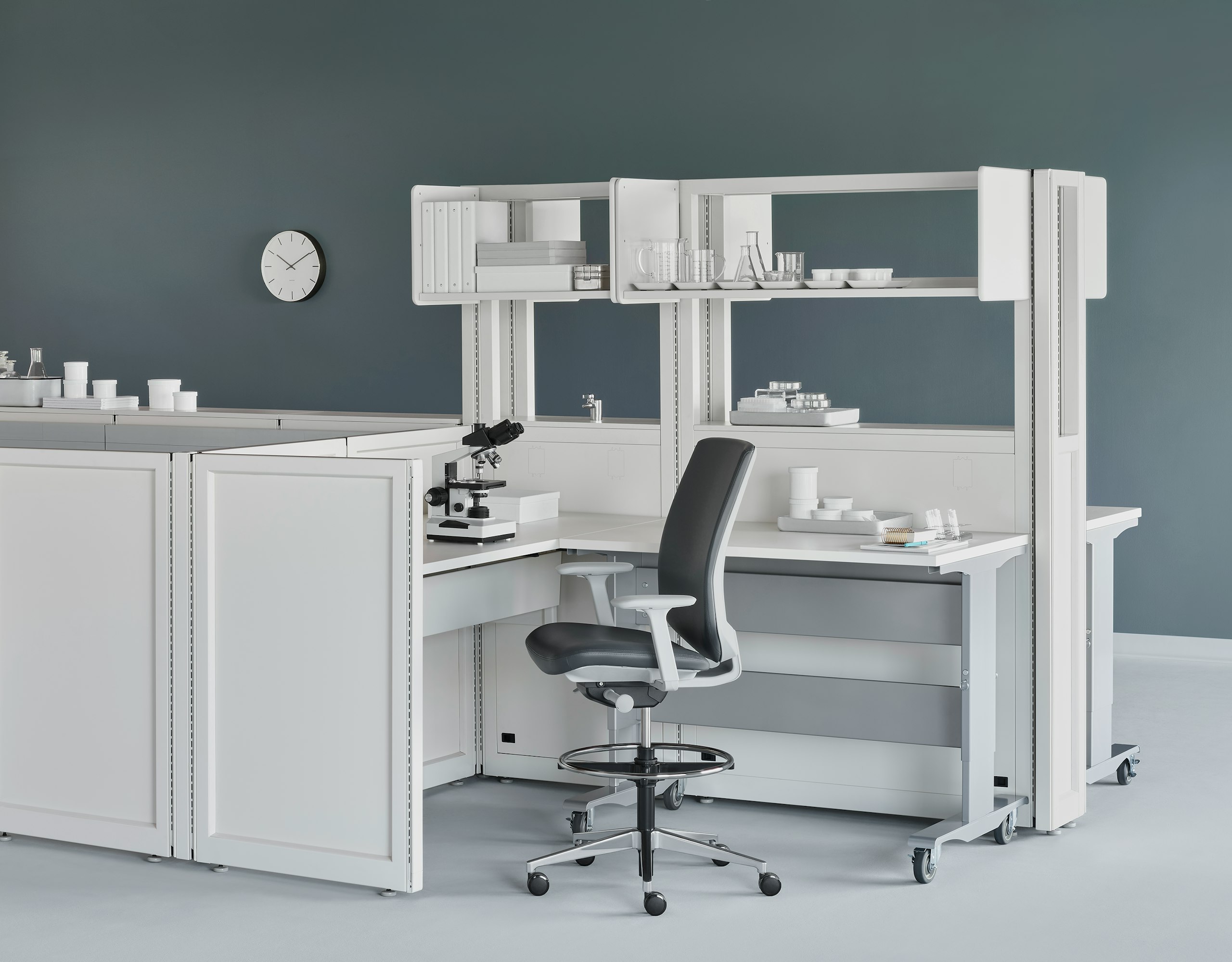 Soft white Co/Struc System with a height-adjustable process table and a dark gray Verus Stool in a medical laboratory.