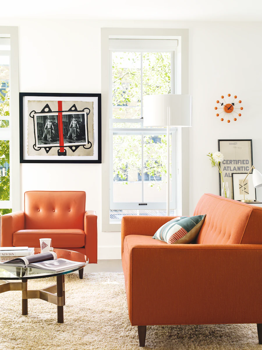 Orange modular sofa and armchairs in a bright modern living room with wall art and floor lamp.