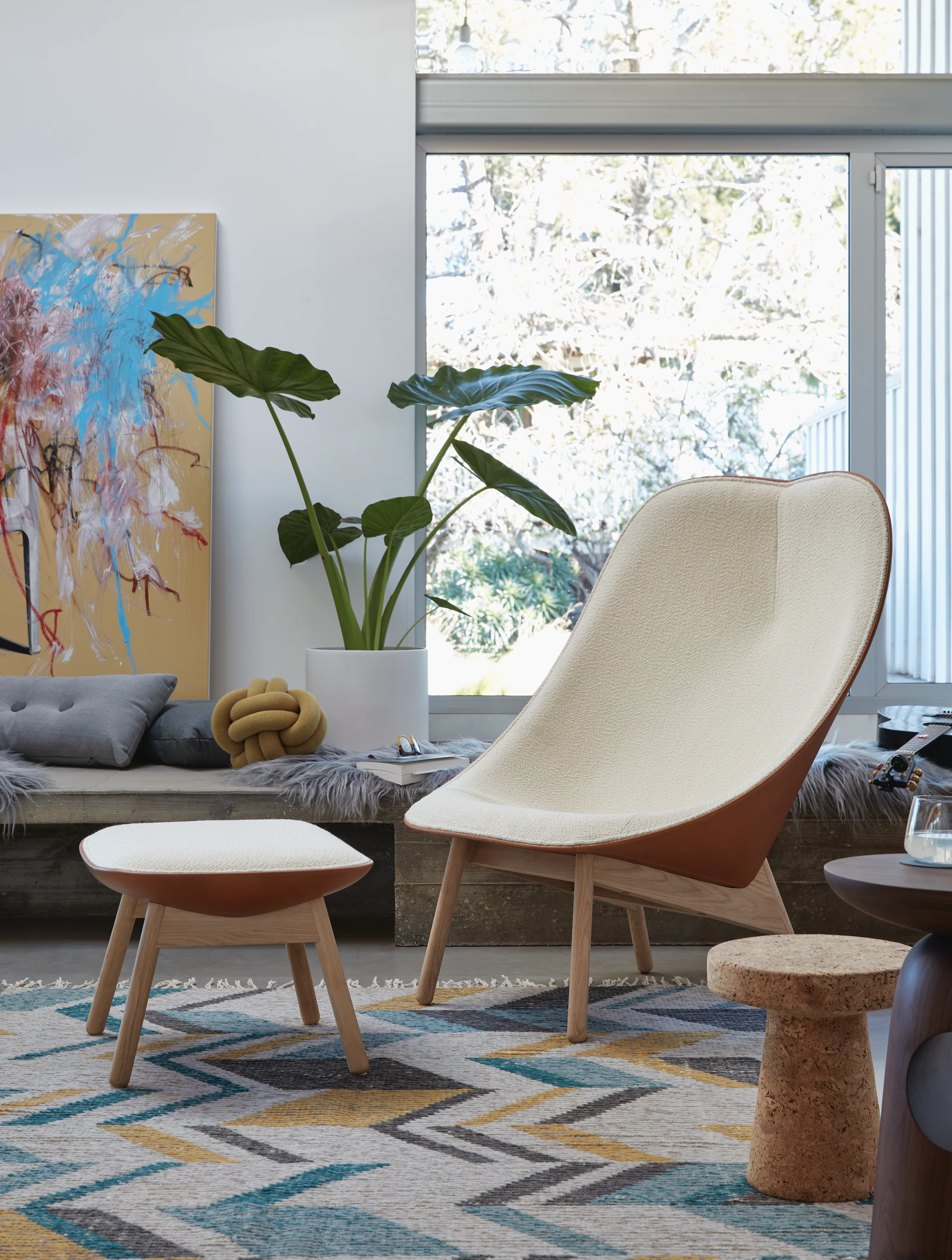 A cream Uchiwa Lounge Chair and Uchiwa Ottoman in a living area with a house plant and artwork.