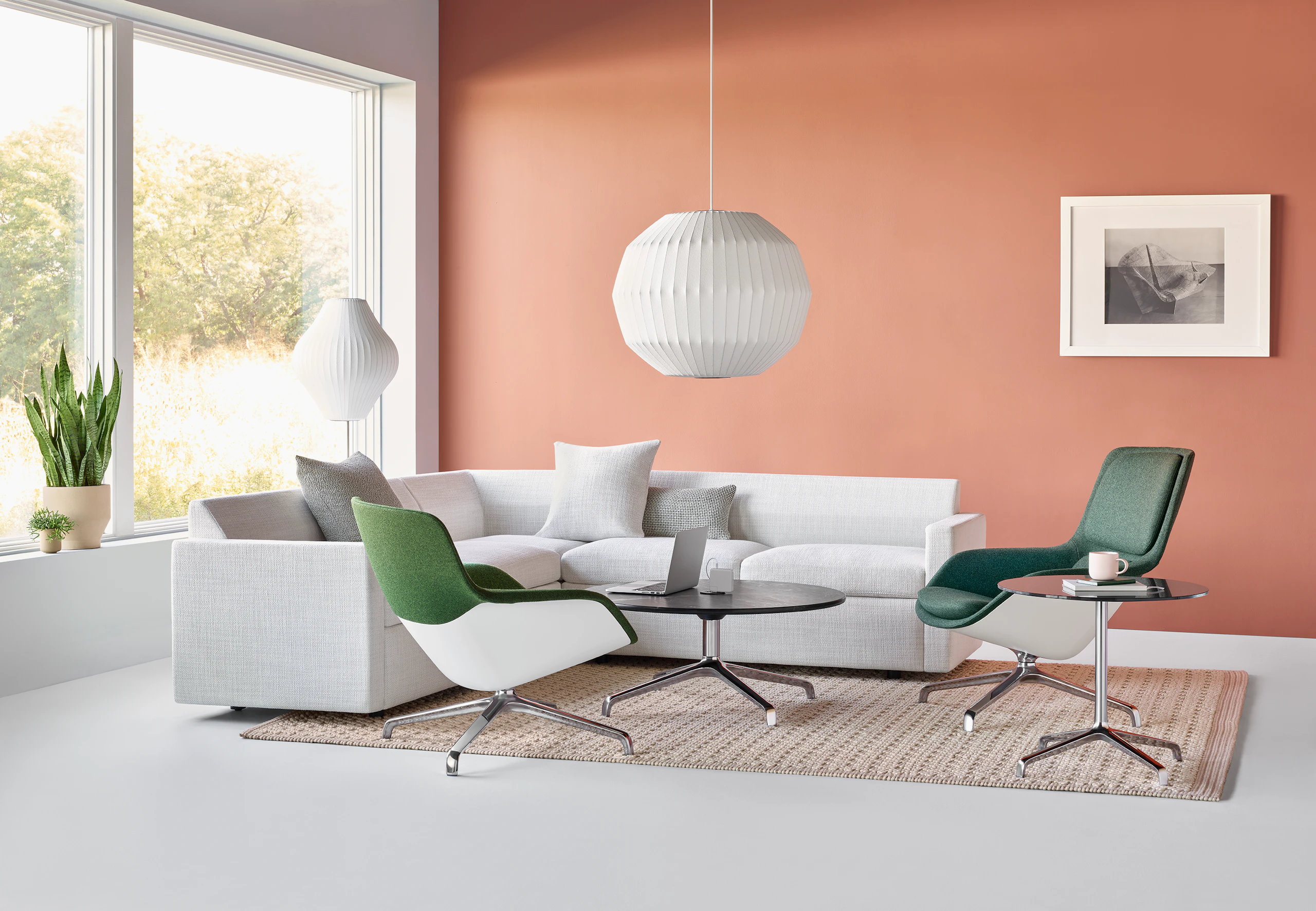 A large Nelson Angled Sphere Bubble Pendant hangs above a casual lounge setting featuring two green Striad Chairs and a white Bevel Sofa set against an orange wall.