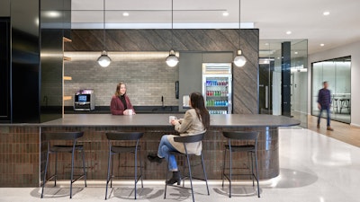 Two people conversing at a large communal kitchen bar furnished with Geiger Leeway Stools at Morning Consult