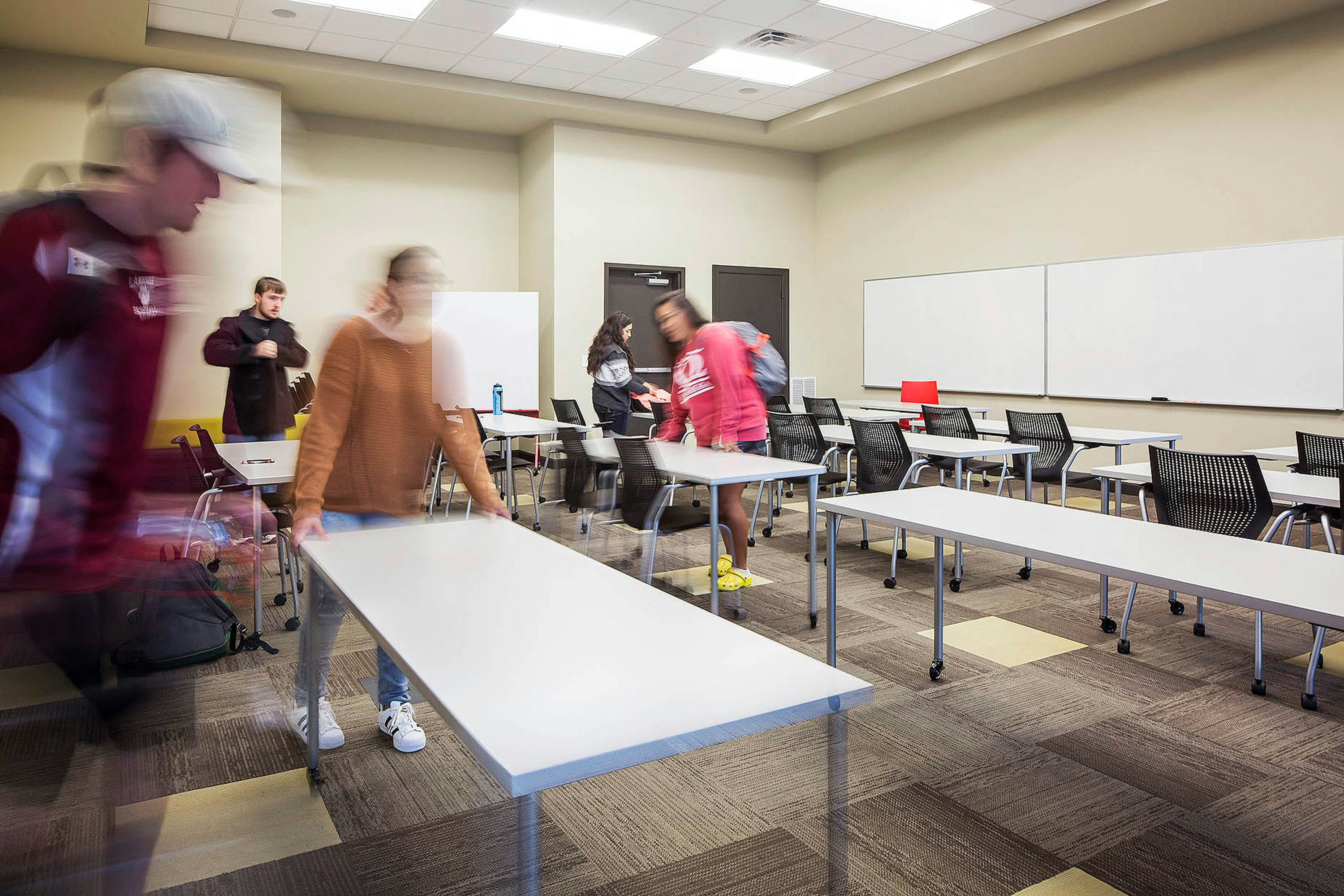 Students rearranging a classroom setting furnished with Antenna Simple Tables and MultiGeneration Chairs.