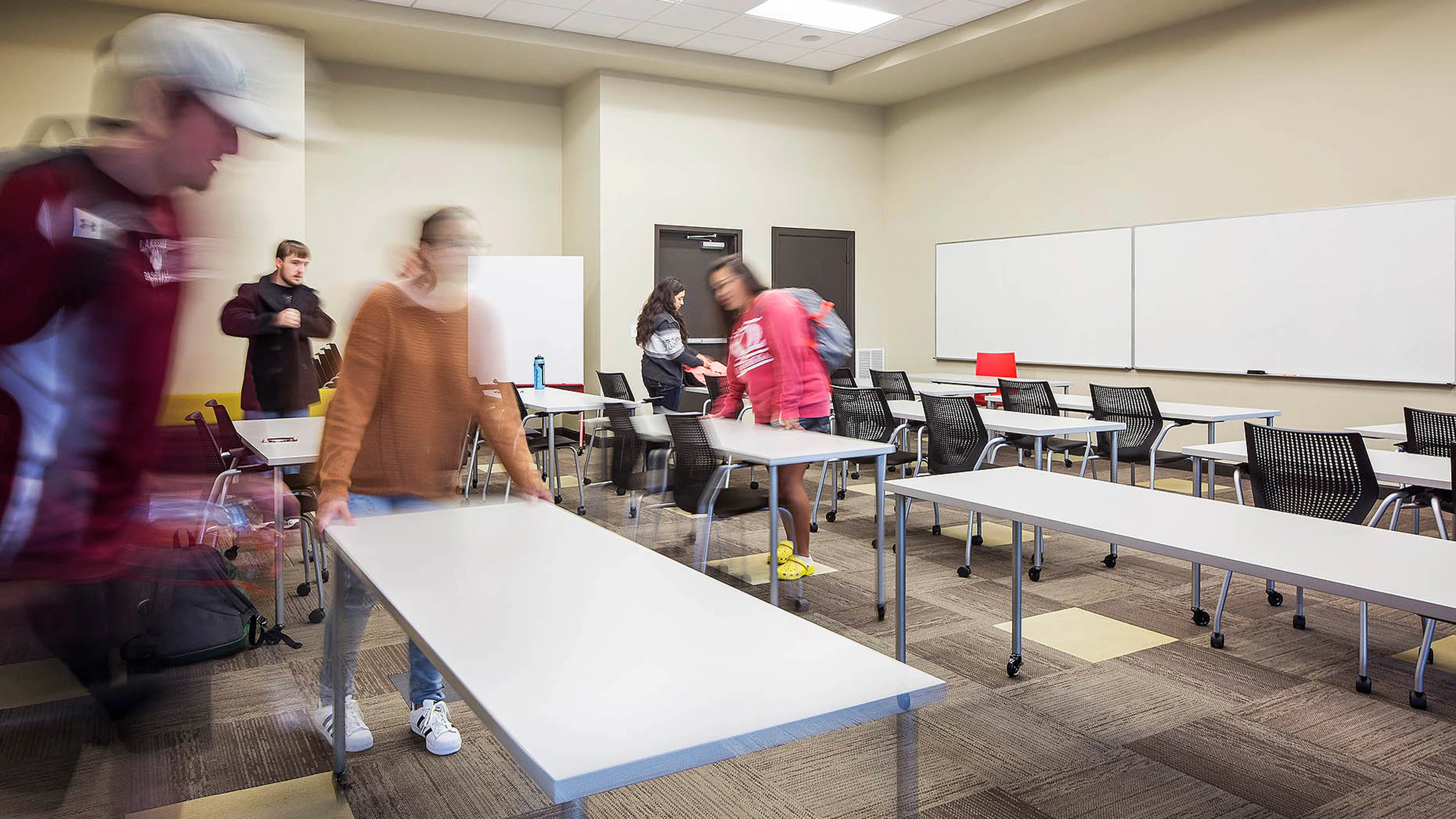 Students rearranging a classroom setting furnished with Antenna Simple Tables and MultiGeneration Chairs.